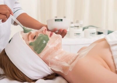 A woman receives a facial treatment with green masks applied to her face in a spa setting.