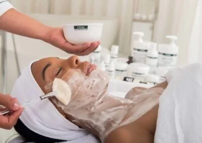 A woman receiving a facial treatment with a mask applied to her face in a spa setting.