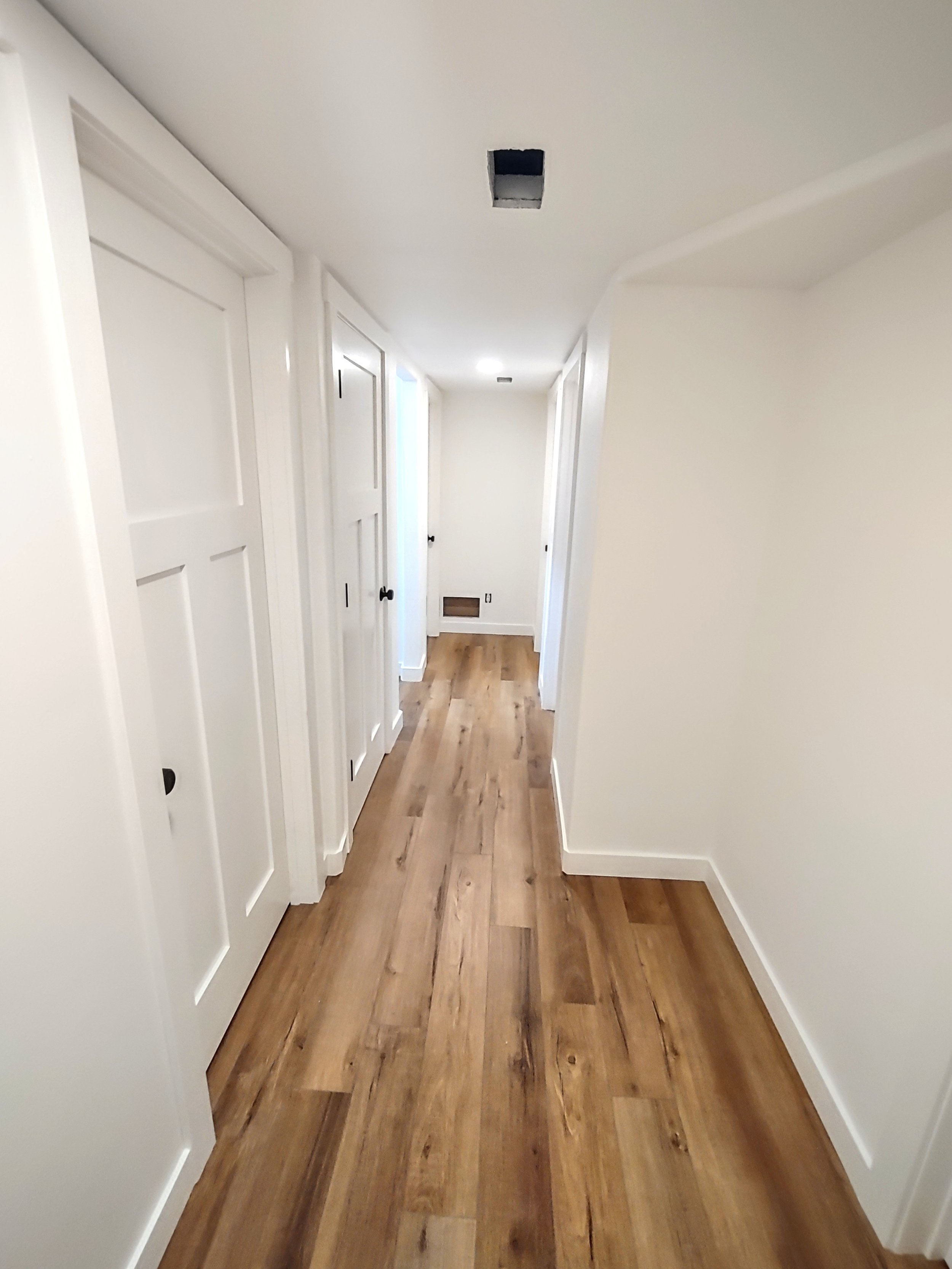 Empty hallway with white walls, wooden flooring, and multiple closed white doors, some with black handles.