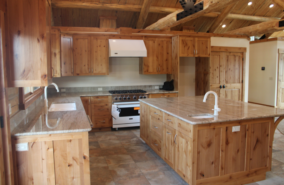 Kitchen with wooden cabinets, granite countertops, a central island sink, and a stove with oven, in a rustic style with wooden ceiling beams.