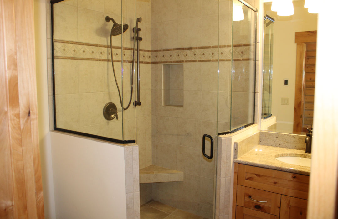 Bathroom with a glass-enclosed shower, beige tiles, a built-in niche, and a wooden vanity with a granite countertop.