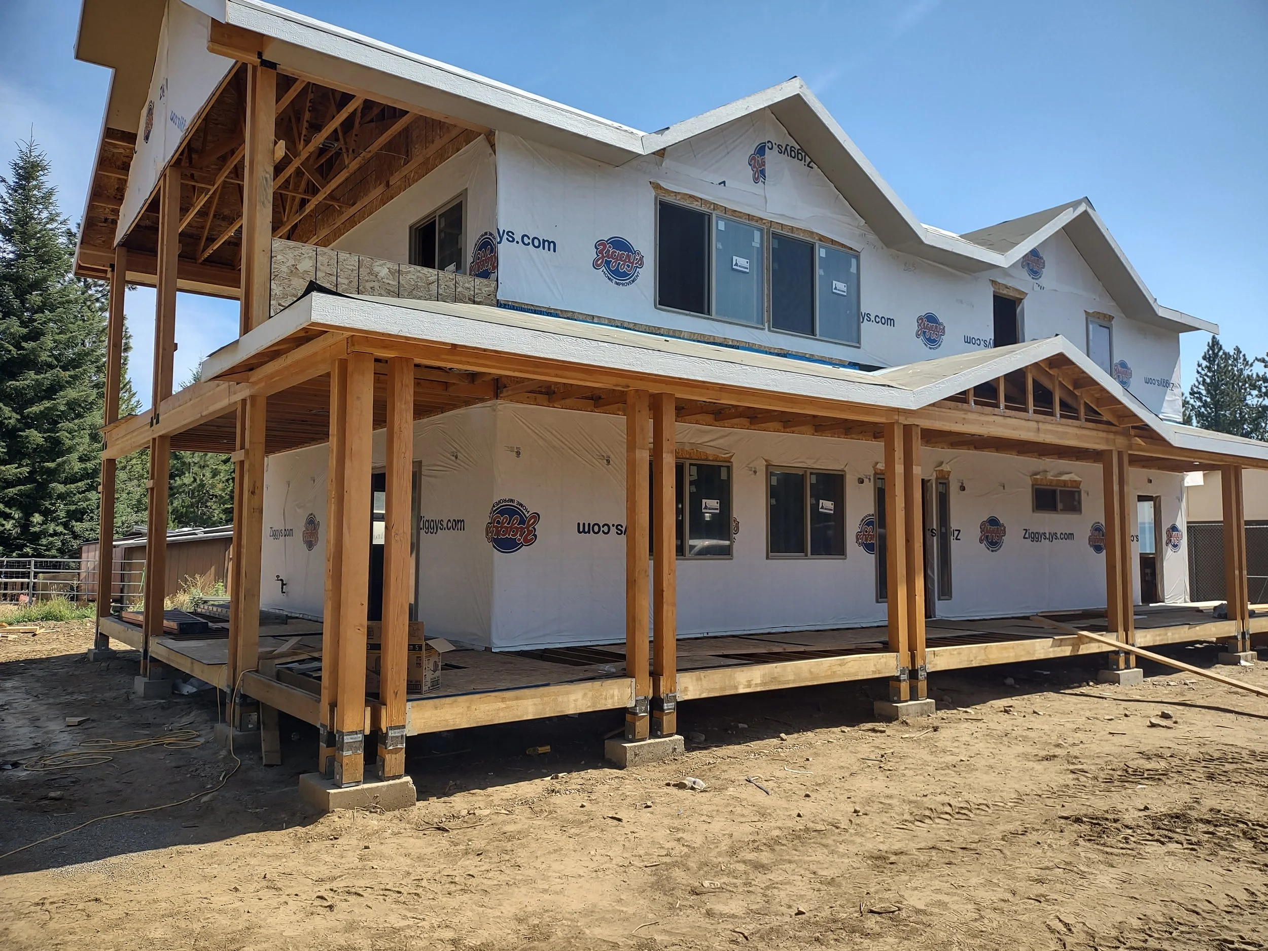 A two-story house under construction with wooden framing, covered in white house wrap with Ziggy's logo, and multiple window openings.