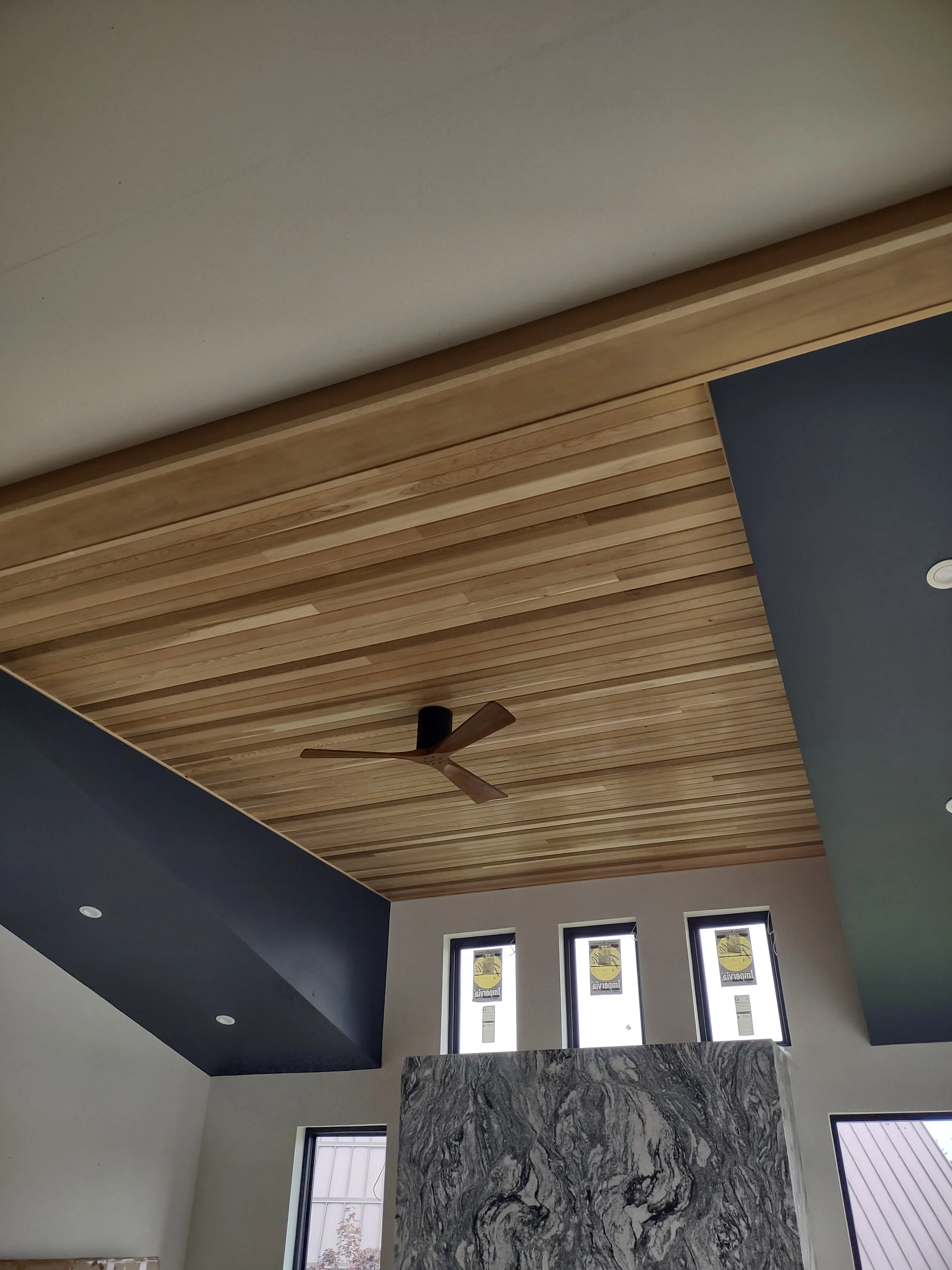 Interior ceiling with wooden planks, a ceiling fan, and high windows, in a modern home or building.