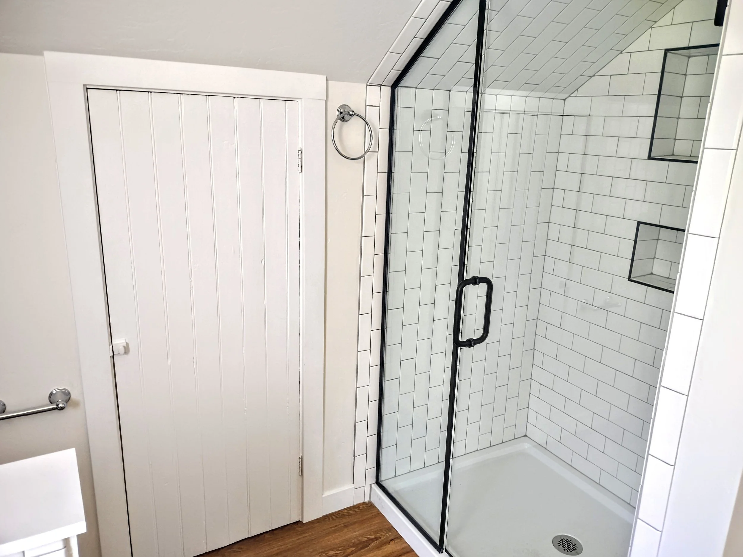 Clean, modern walk-in shower with white subway tiles, two built-in shelves, a black framed glass door, and a white tiled floor.