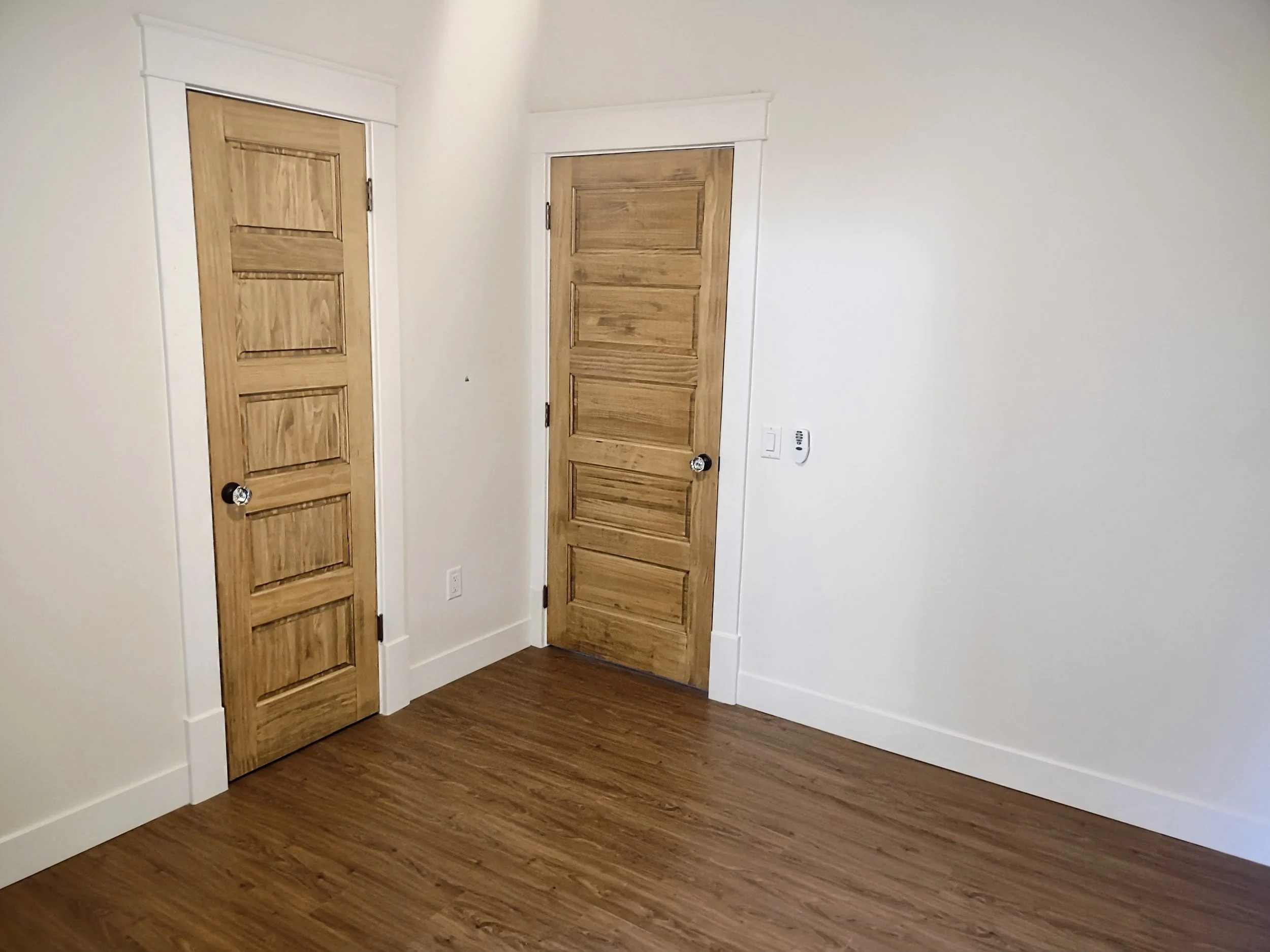 Empty room with white walls, wood floor, and two wooden doors.
