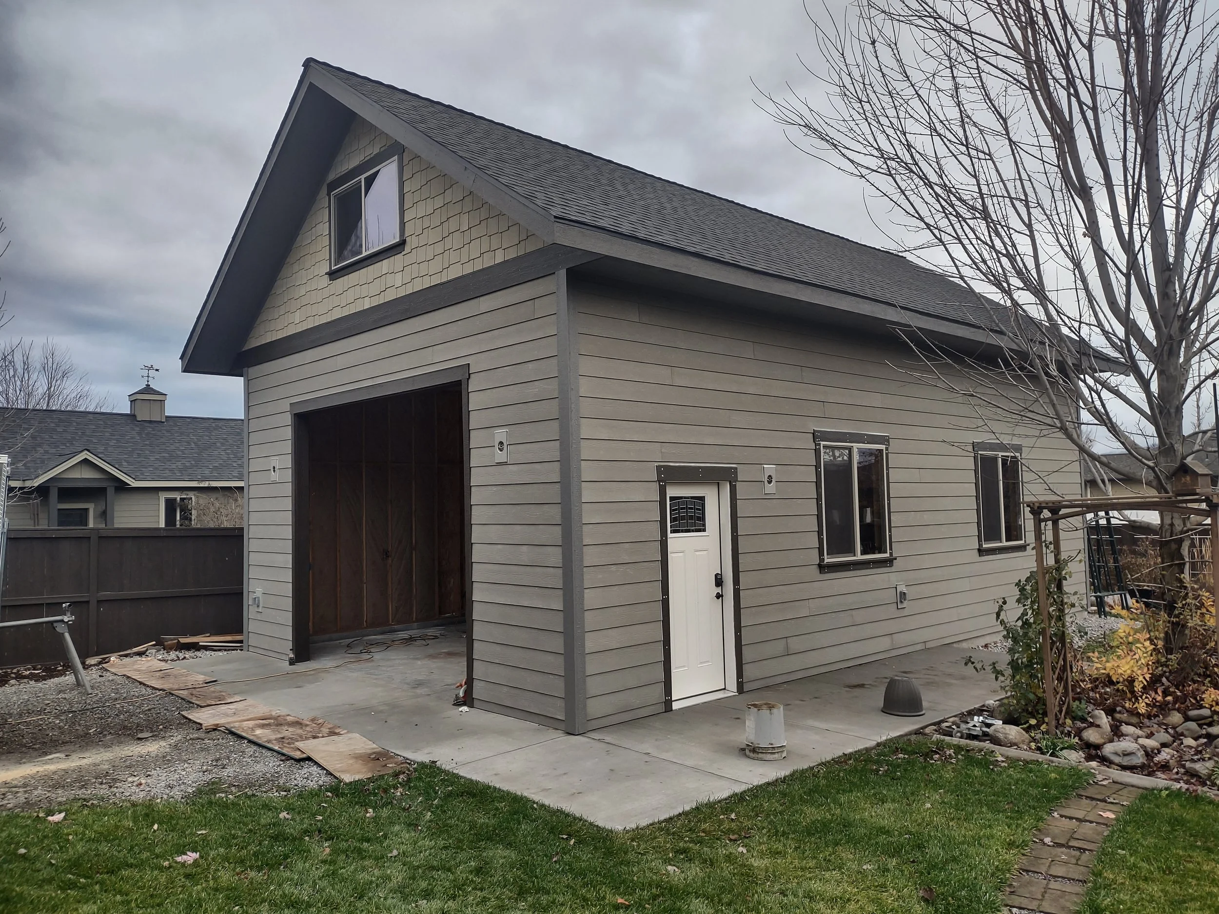 A house with vinyl siding, a garage opening, and a small side door, with a tree and a lawn in the yard.