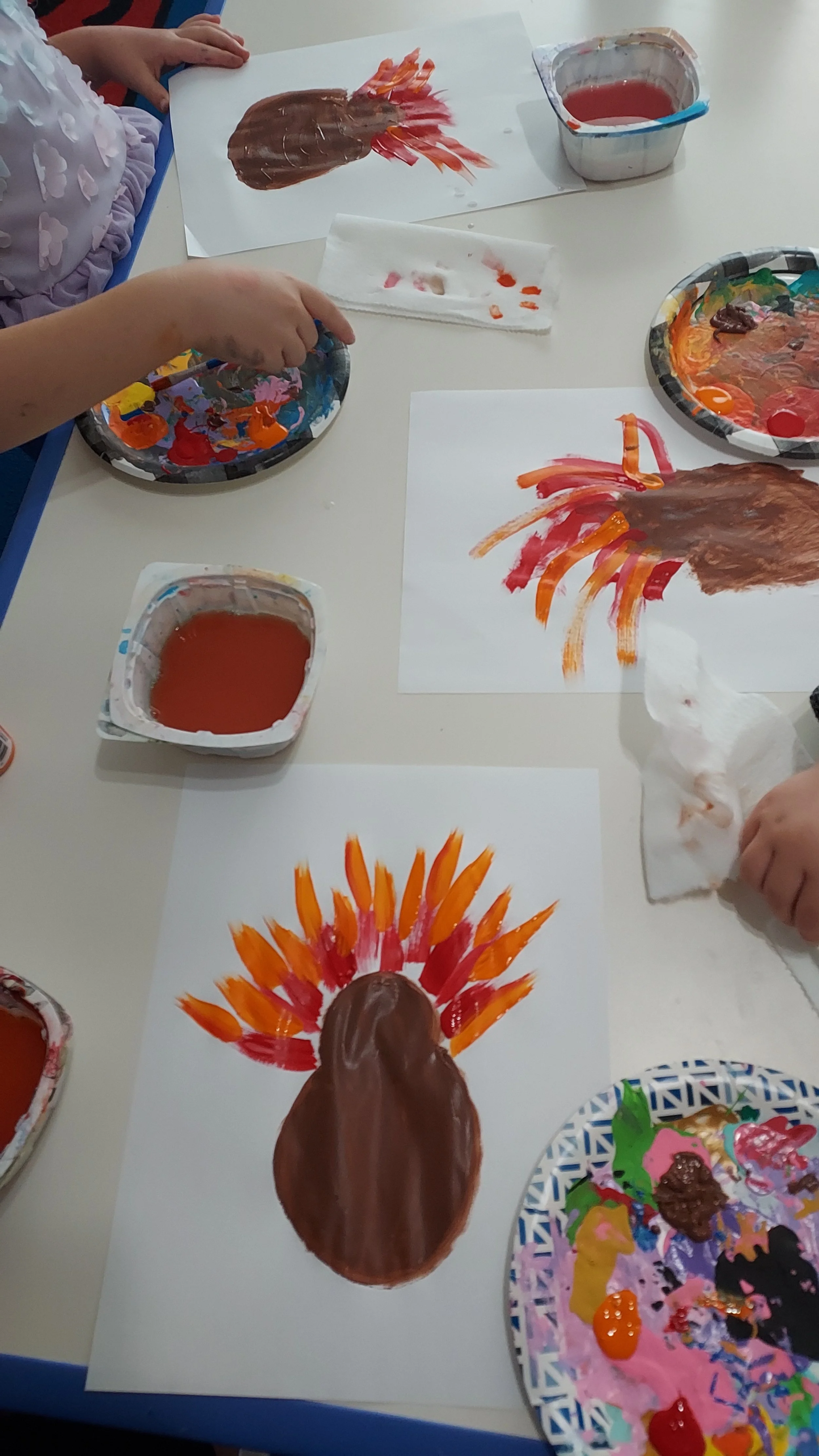 Children painting turkeys with brown and orange paint on paper.