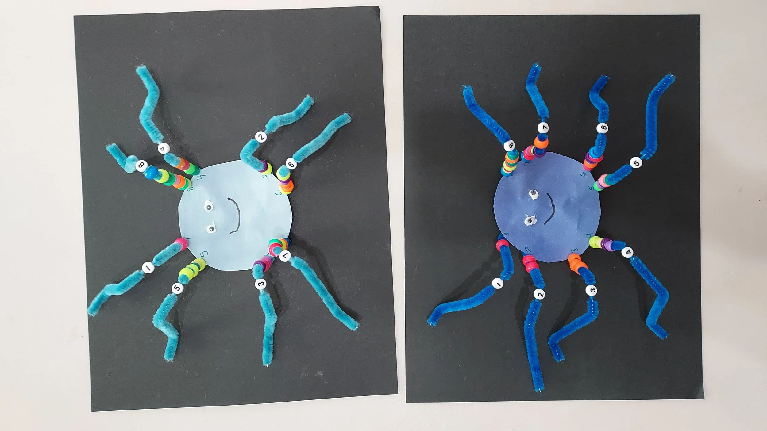 Two craft projects of crab shapes made from blue paper circles with pipe cleaner legs on black construction paper backgrounds.
