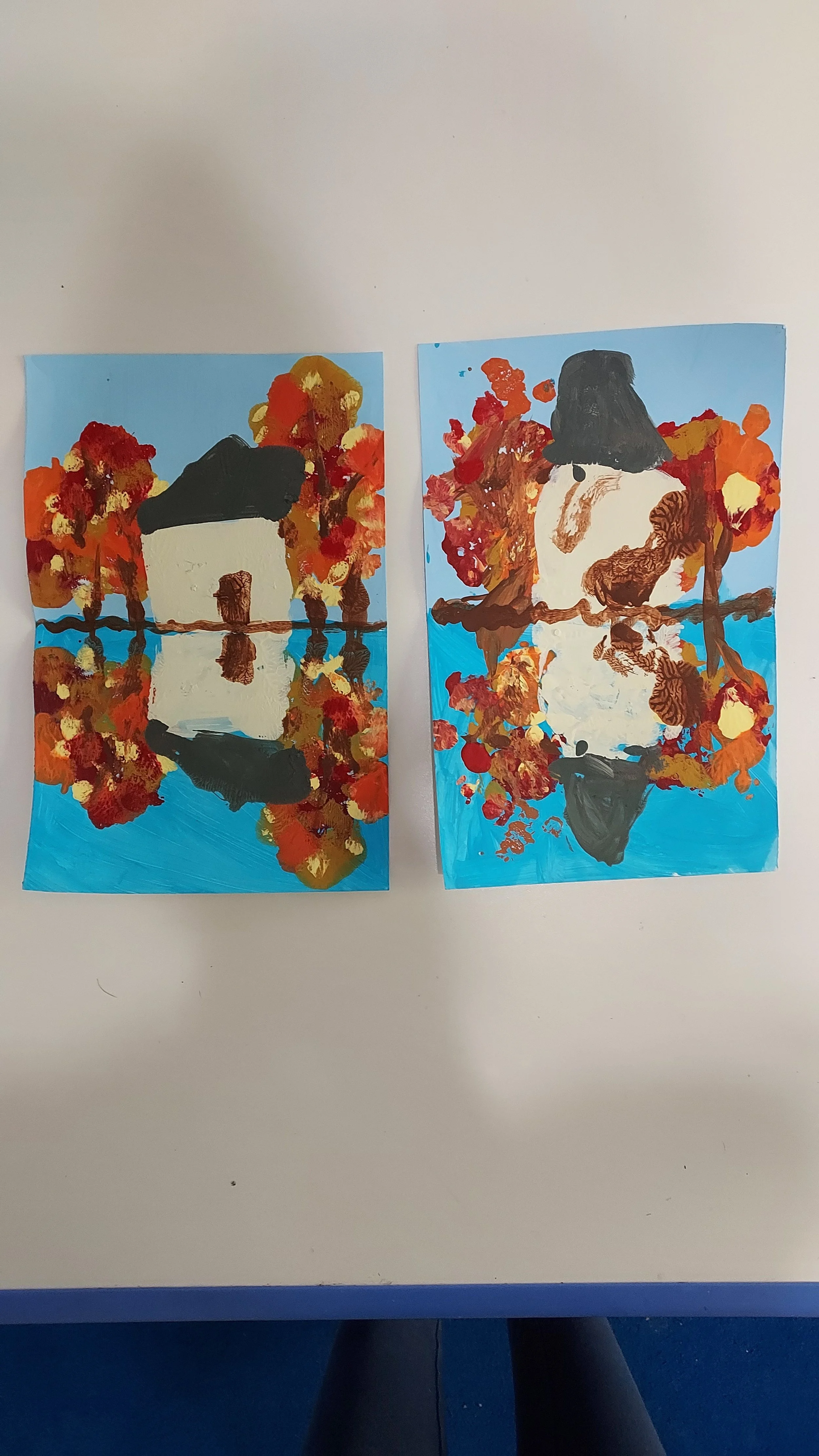 Two colorful paintings of women with long hair, reflected in water, surrounded by vibrant autumn leaves, on a blue background.