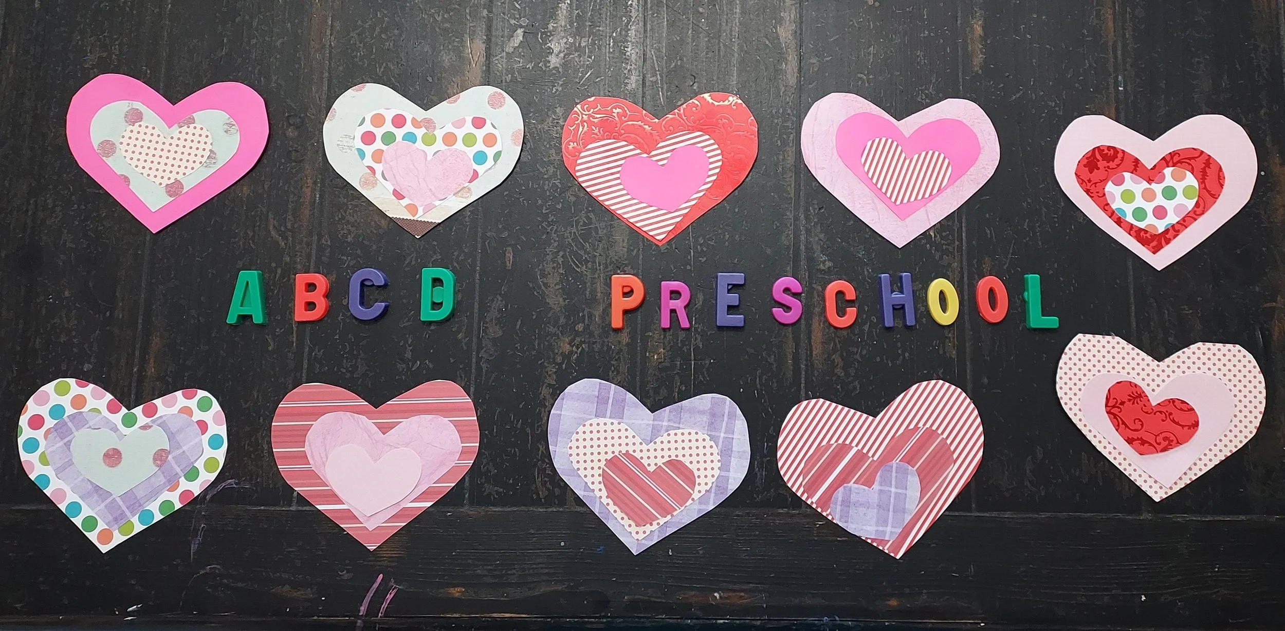 Colorful paper hearts and foam letters spell out 'ABC D PRE SCHOOL' on a dark wooden surface.