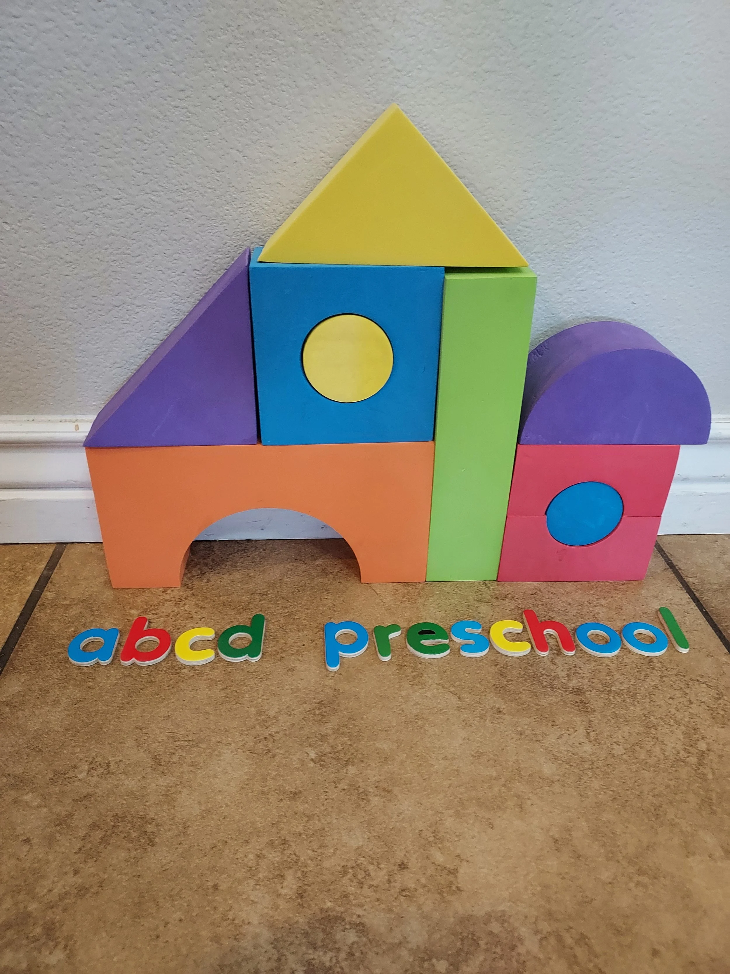 Colorful toy blocks arranged to resemble a miniature house, with the words 'abc d preschool' spelled out in multicolored letters on the floor.