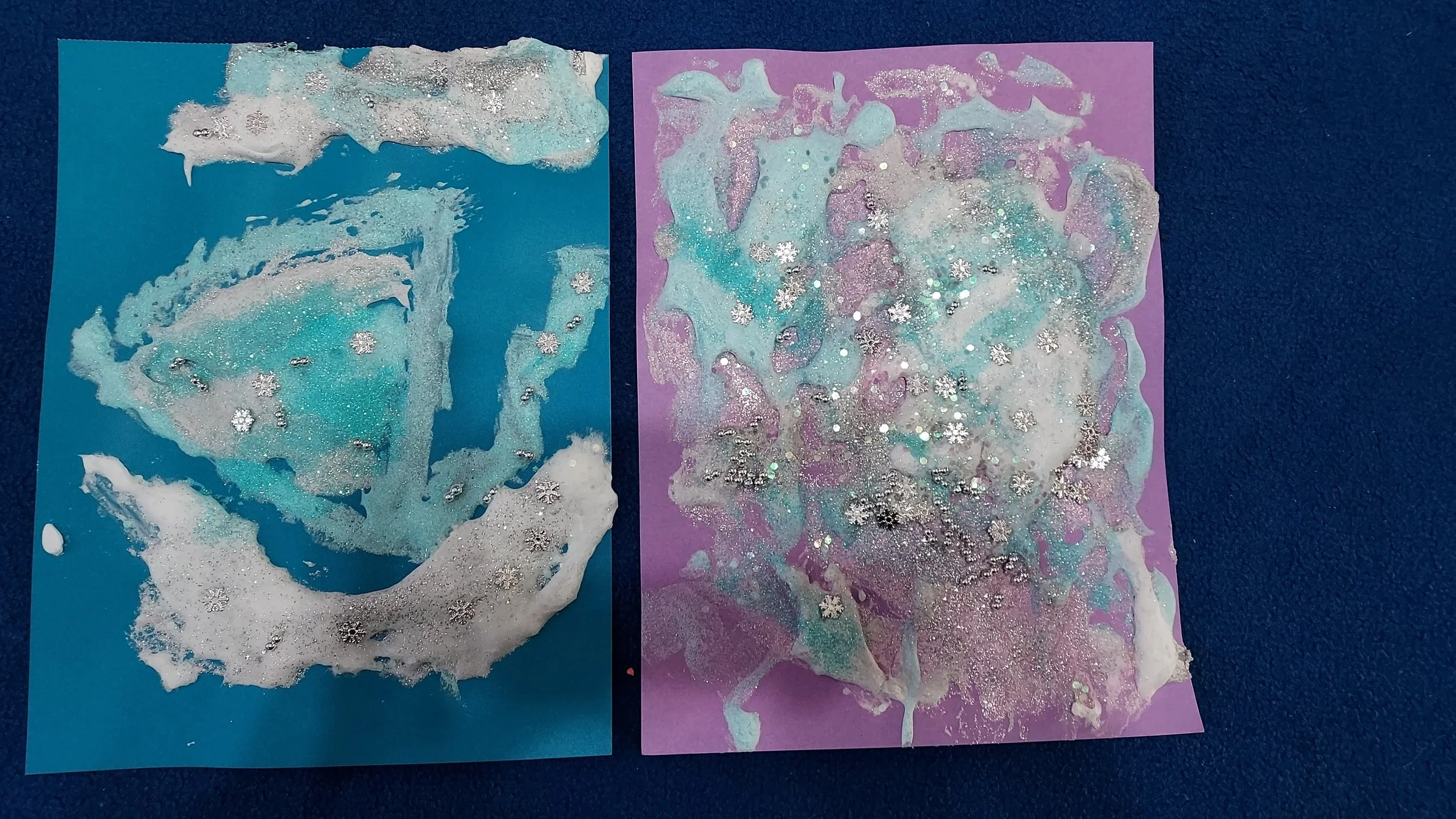 Two colorful abstract art pieces on blue and purple paper with silver and white glitter and snowflake-shaped embellishments.