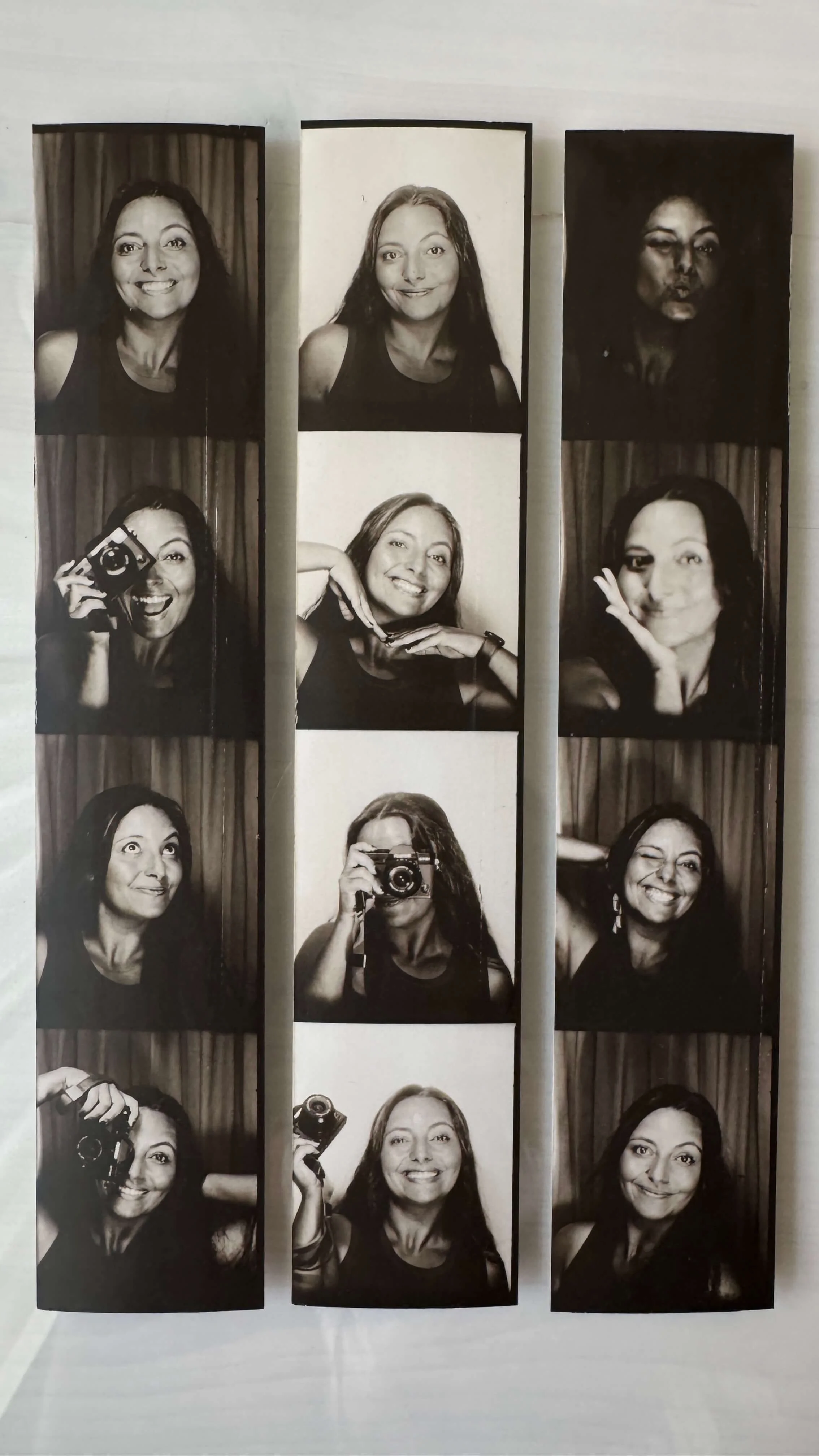 Set of black-and-white photo booth strips featuring a woman making different expressive poses, including holding a camera, smiling, and winking, with a curtain background.