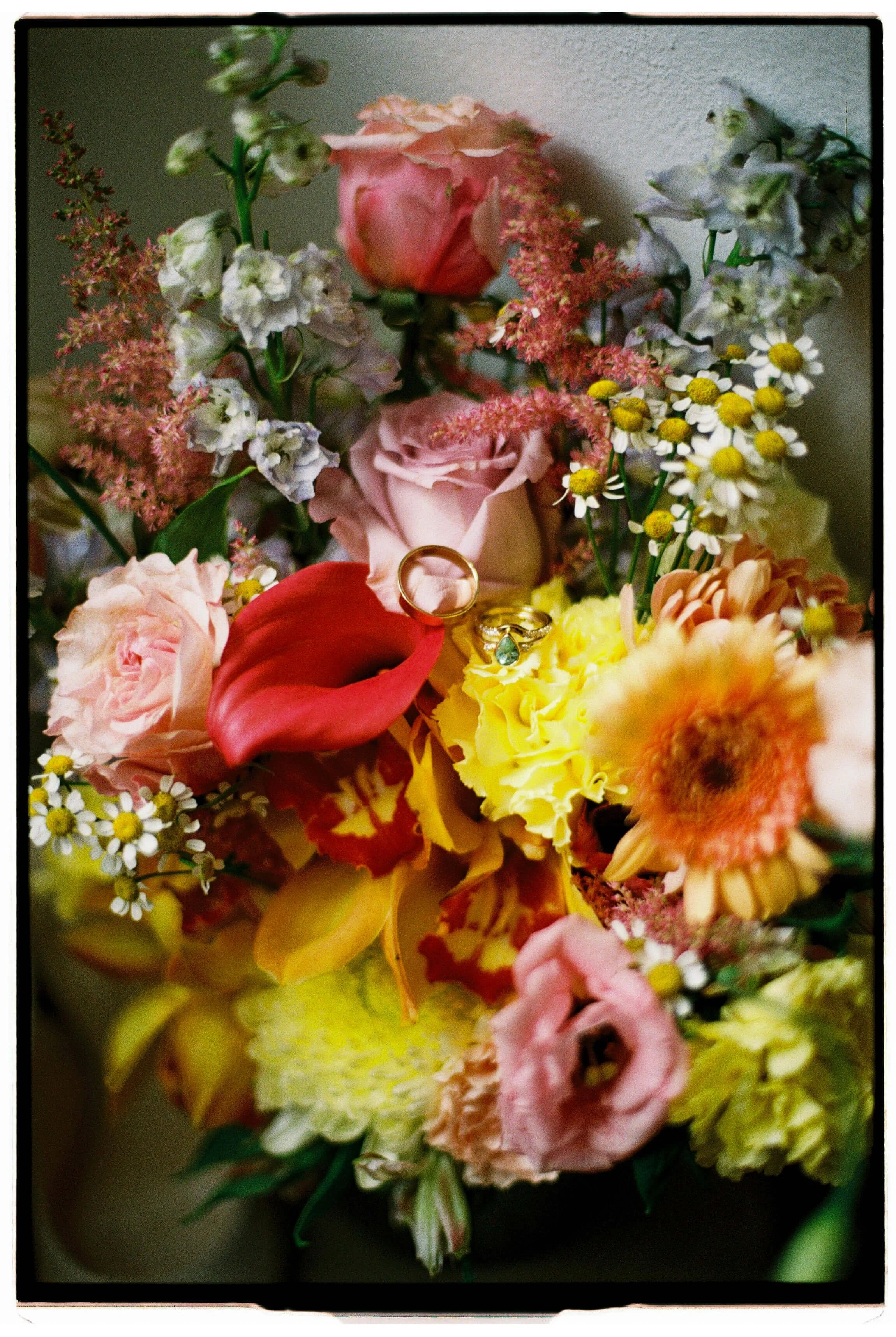 A colorful bouquet of mixed flowers with two gold rings placed among the blossoms.