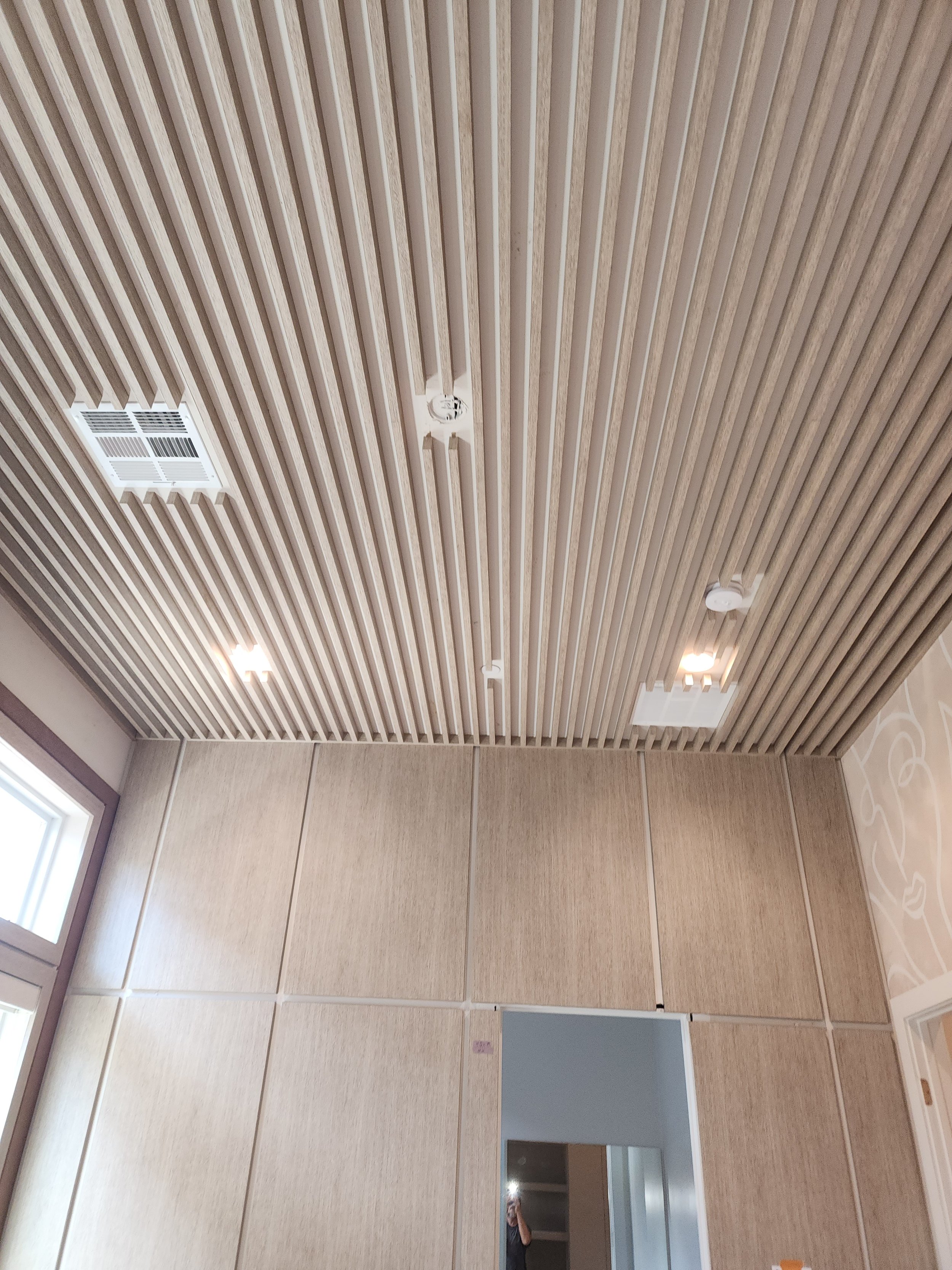 A ceiling with wooden slats, ventilation grilles, and light fixtures in a modern interior space.