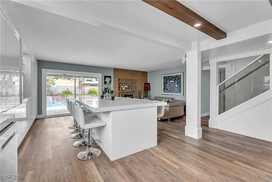 Open-concept living space with kitchen, bar seating, and sitting area, sliding glass door to backyard with pool and outdoor furniture, staircase, and contemporary decor.