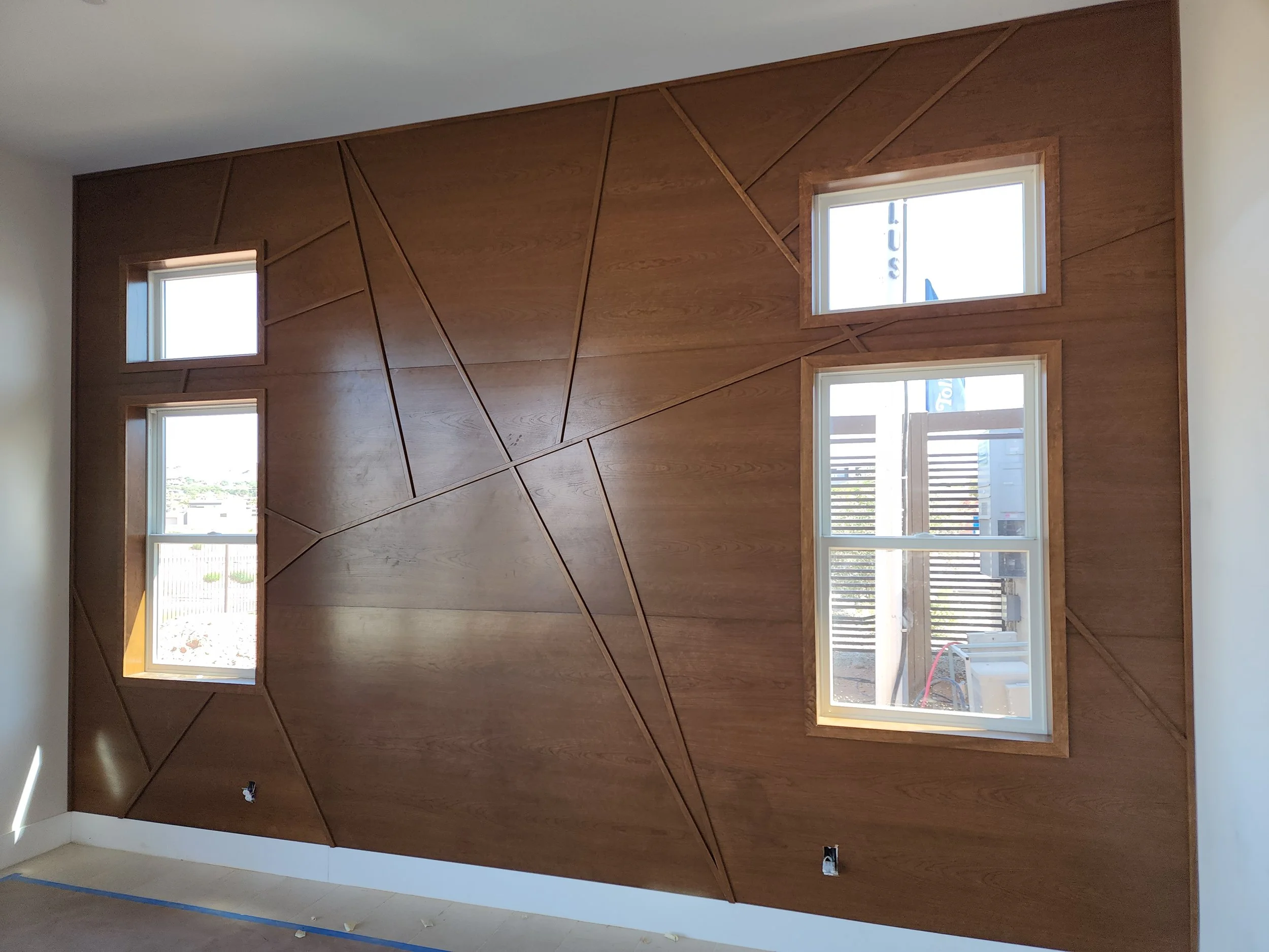 Interior of a room with a wooden accent wall containing geometric patterns and four small windows, with electrical outlets below.