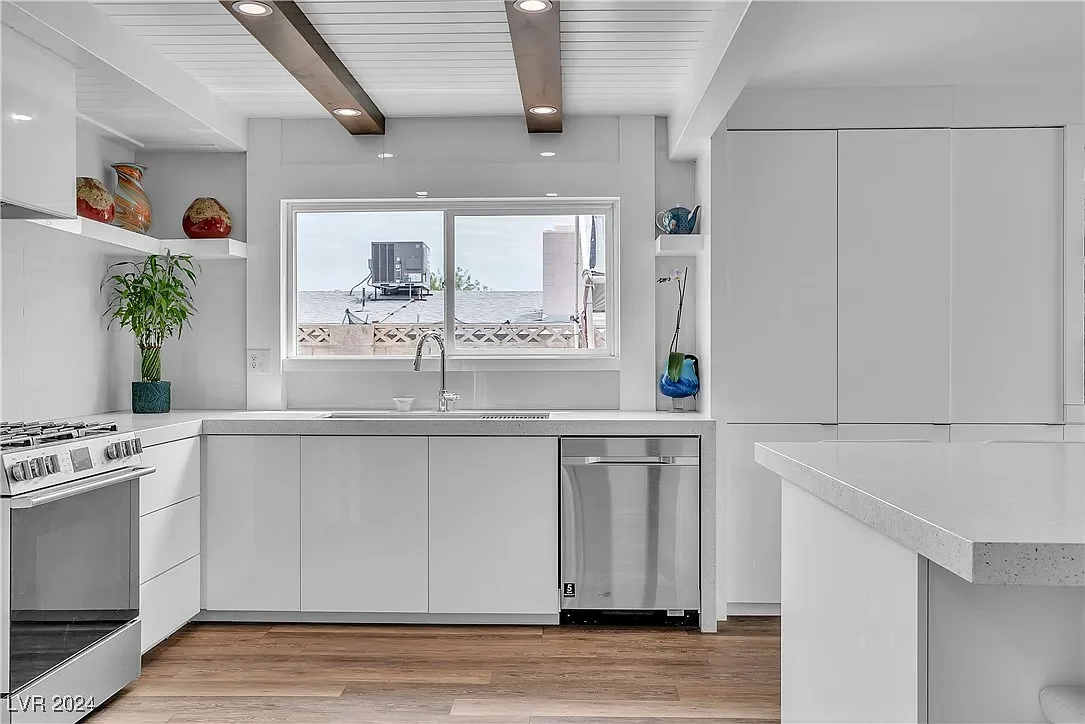 Modern kitchen with white cabinets, a window with a view of neighboring rooftops, a stove, a plant, and decorative vases.