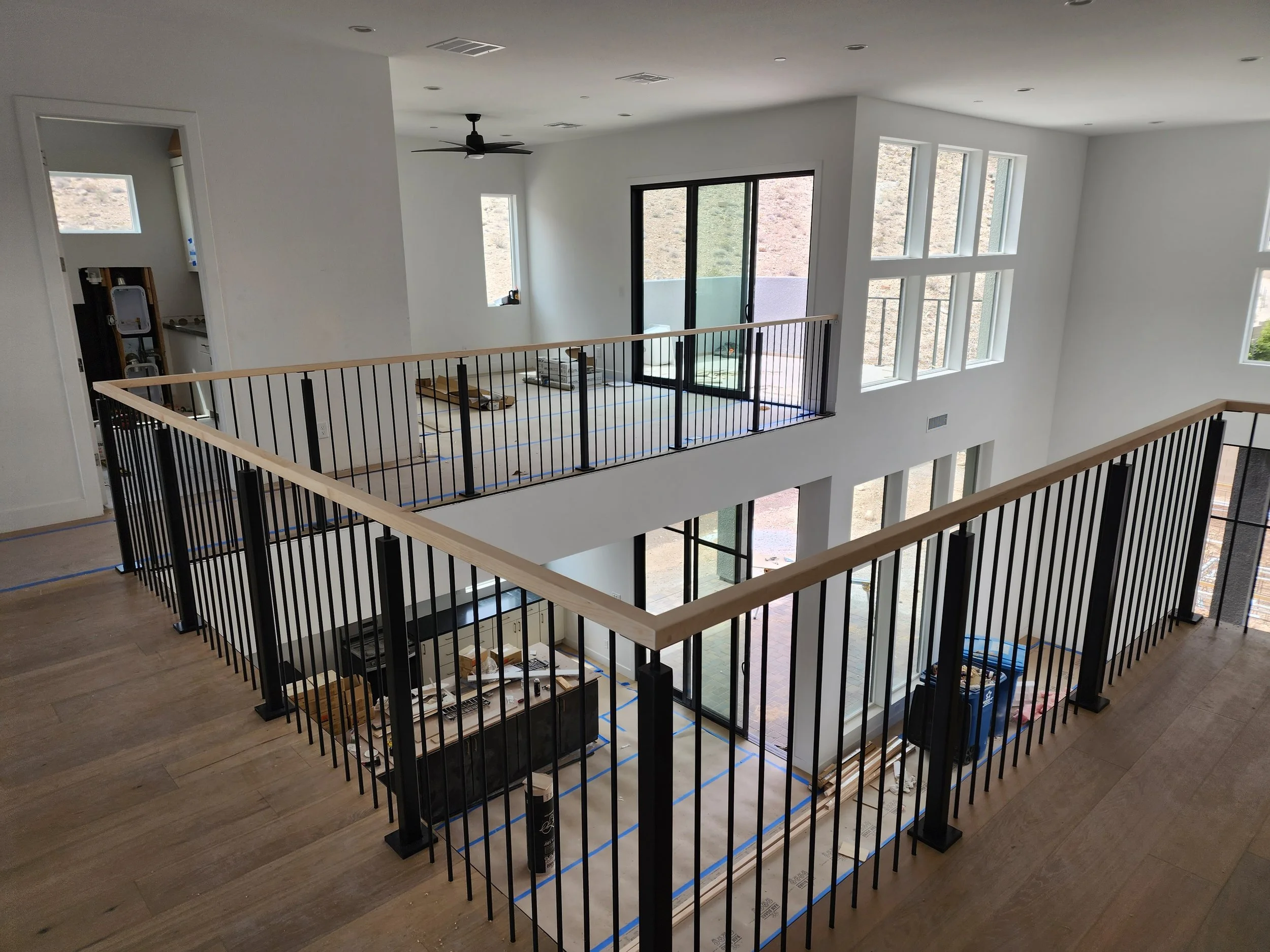 Interior of a modern house under construction with open balcony, large windows, white walls, and black railing.