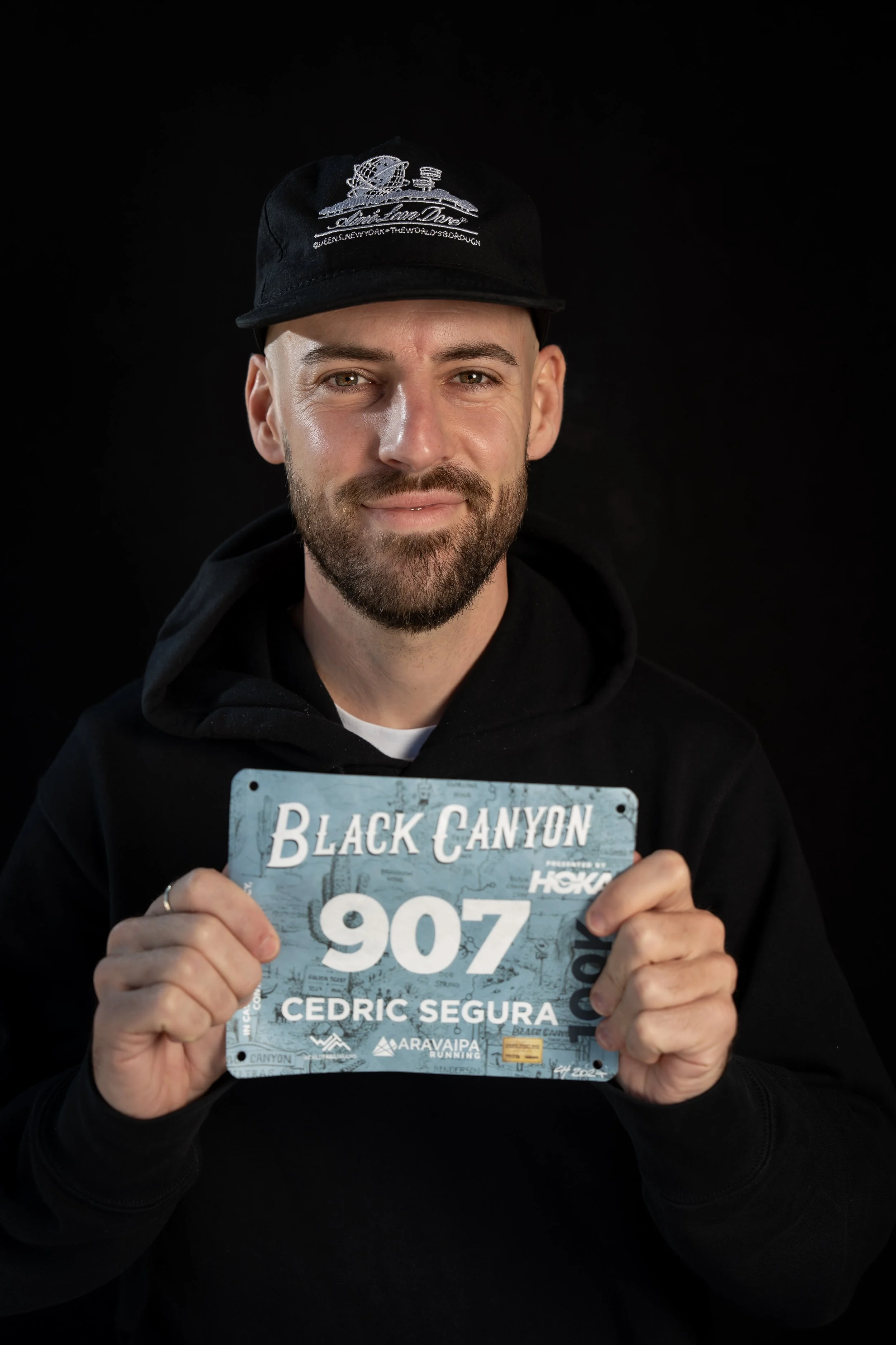 Cedric tenant le dossard 907 de Black Canyon 100k 2025 contre un fond noir.