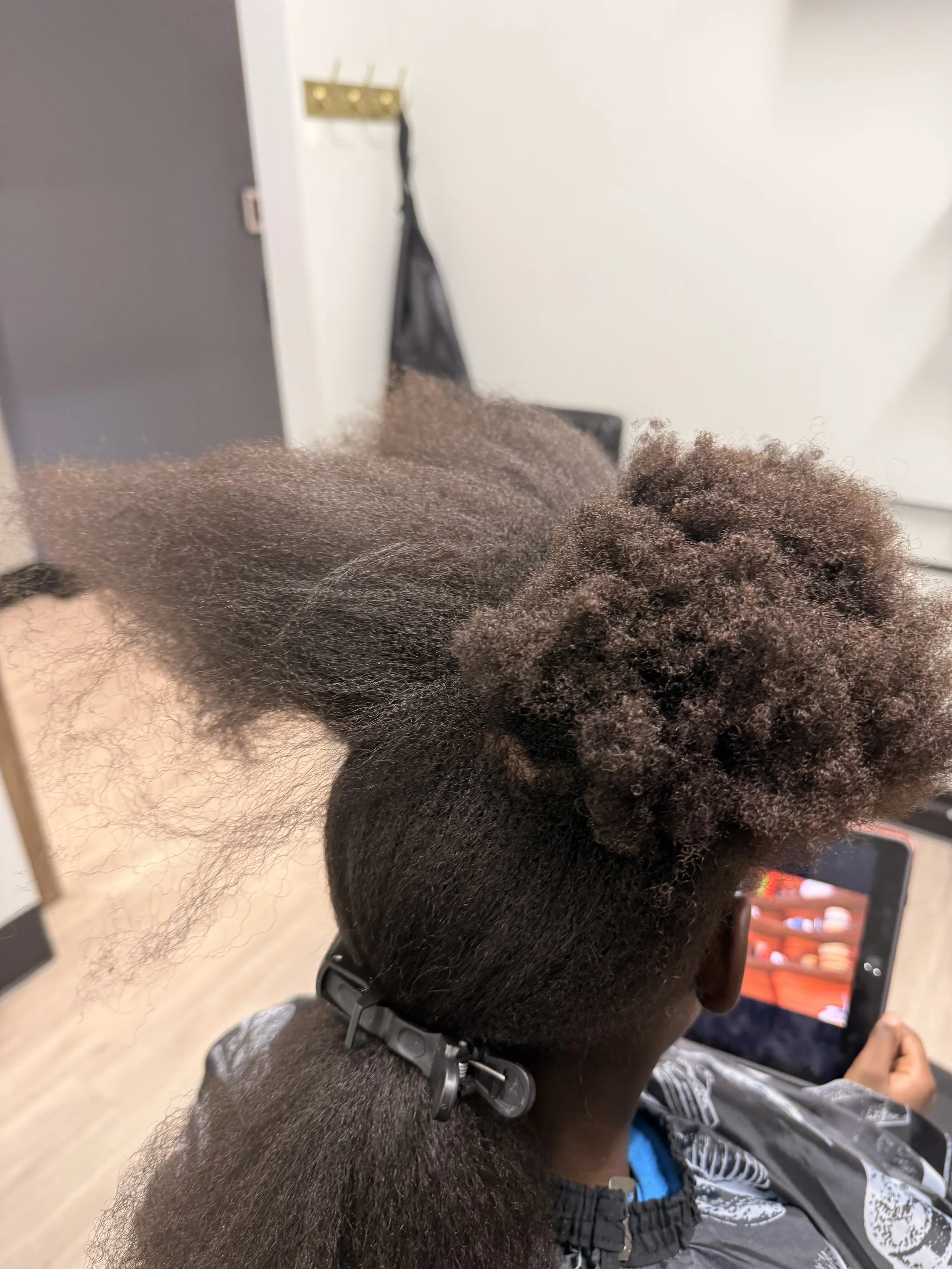 Person getting a natural hair full relaxer treatment in a salon, with hair sectioned and waiting to be smoothed.
