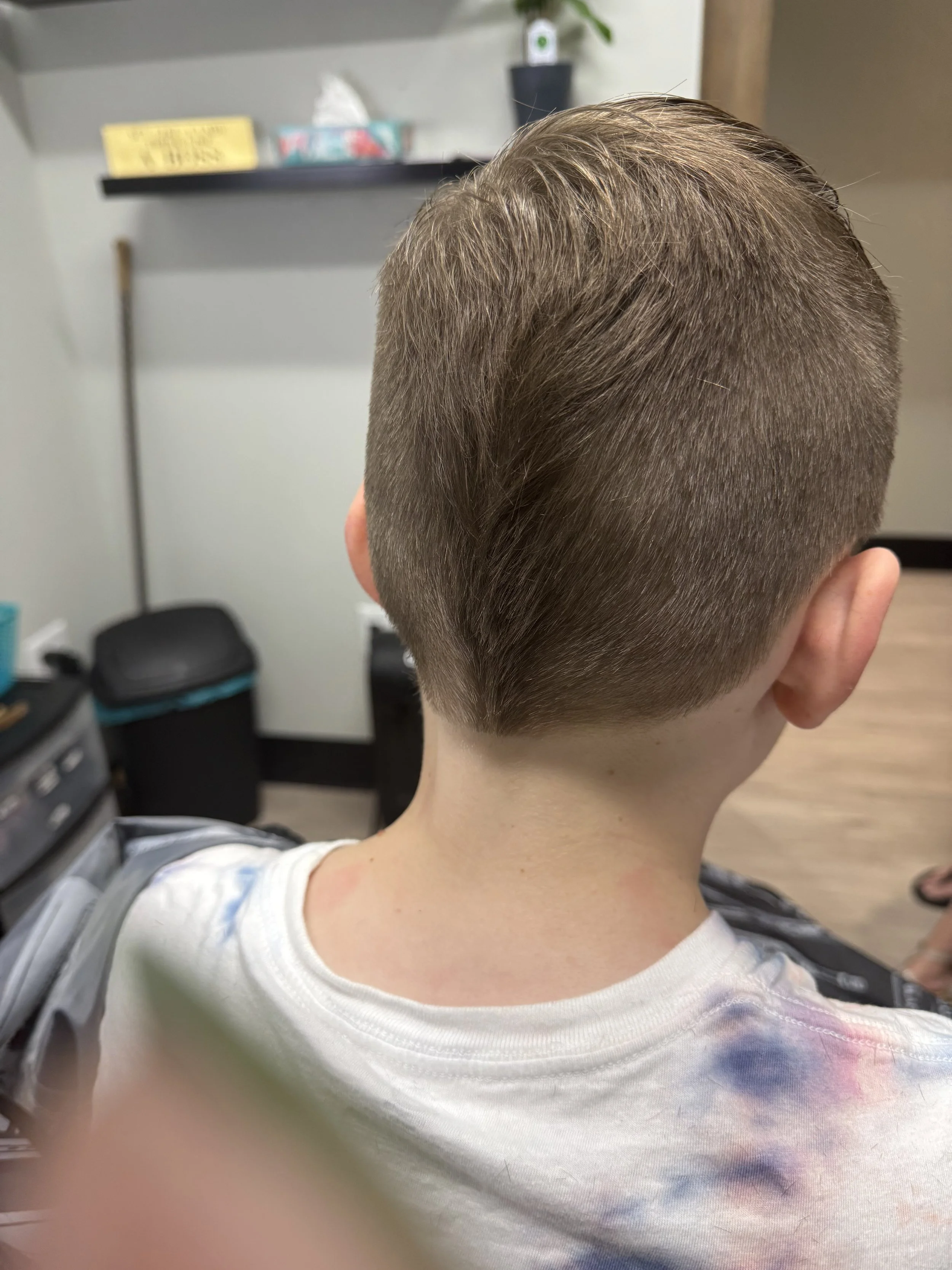 Back of a boy's head showing a new haircut with short sides and longer top, in a barbershop.