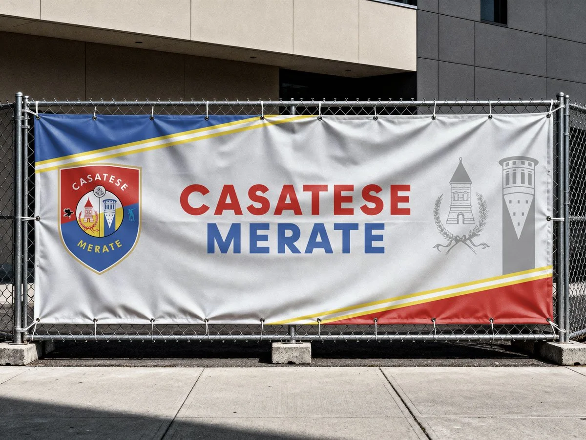 Banner con il logo di Casatese Merate e l'iscrizione 'Casatese Merate' in rosso e blu, installato su una recinzione in metallo davanti a un edificio moderno.