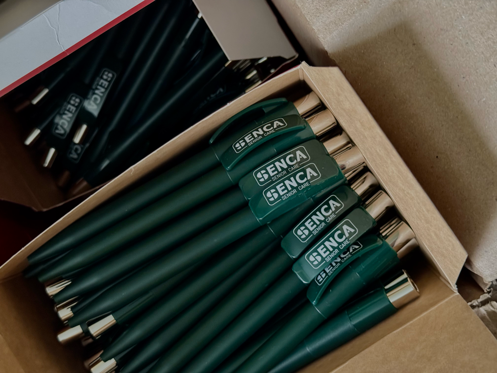 Pennarelli verdi con scritta 'SENCA Senior Care' in una scatola di cartone