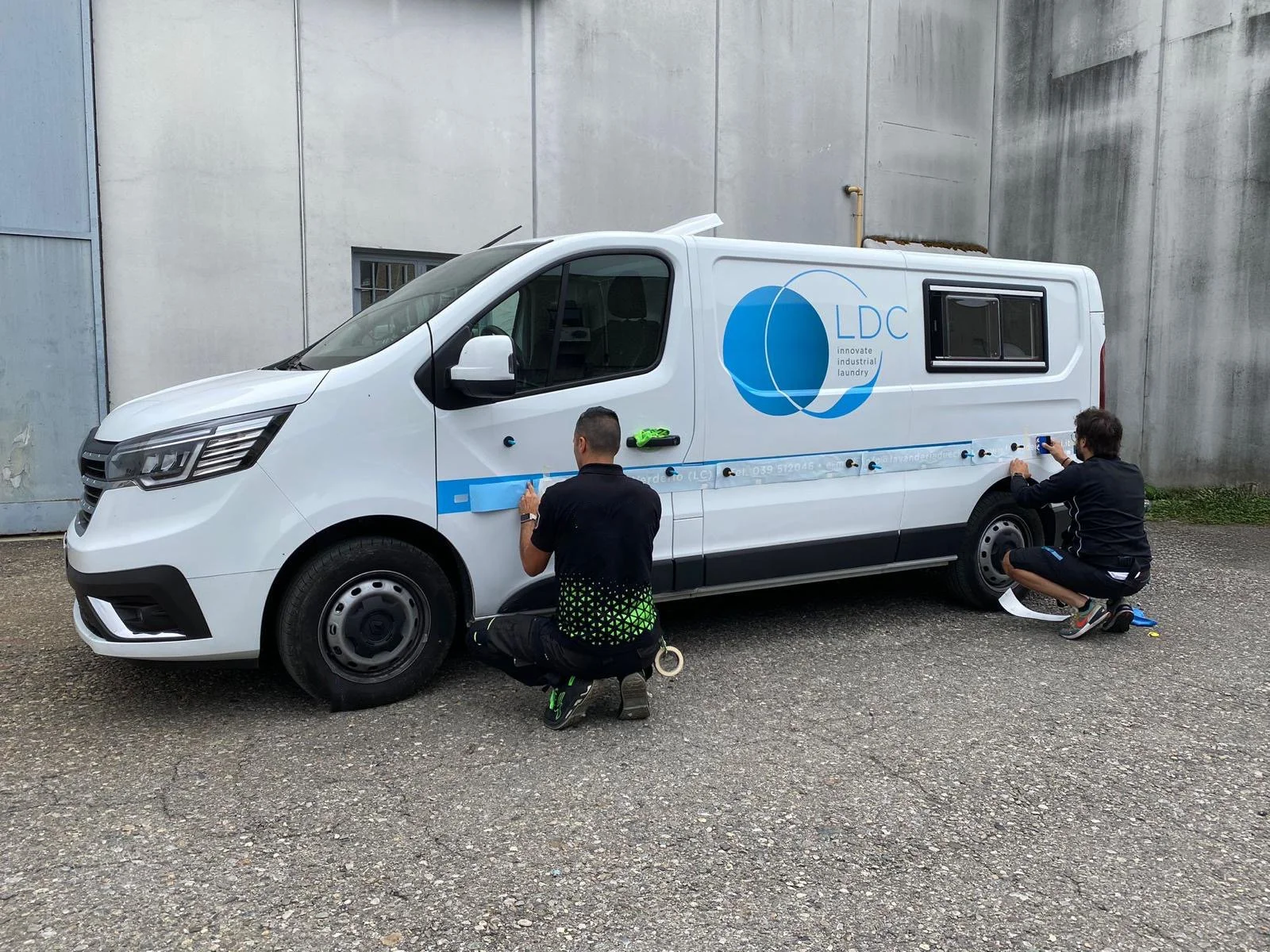 Due uomini stanno applicando adesivi personalizzati sulla fiancata di un furgone.