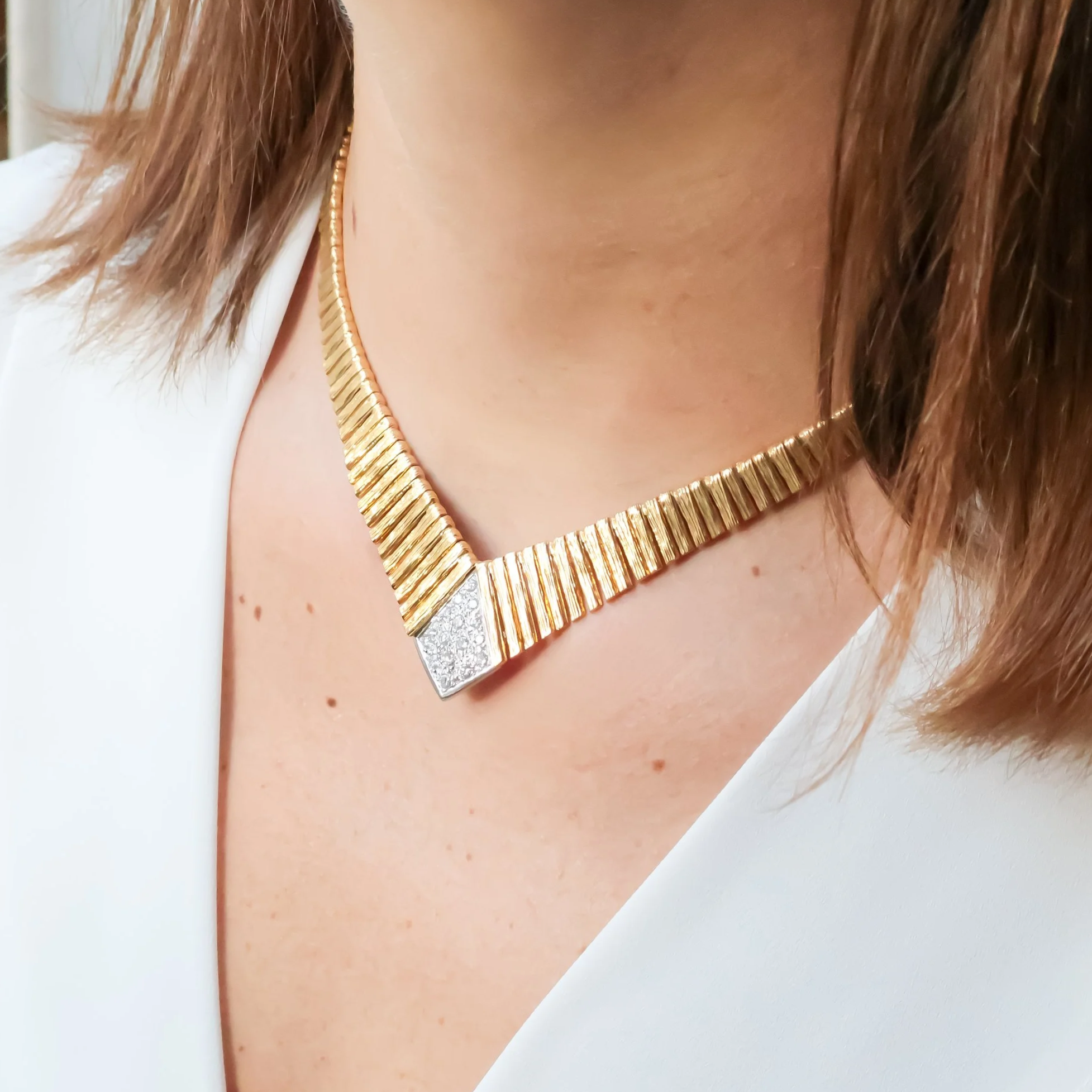 Collier doré avec une pointe argentée en diamant dans le centre, porté par une femme avec des cheveux châtains, portant un vêtement blanc.
