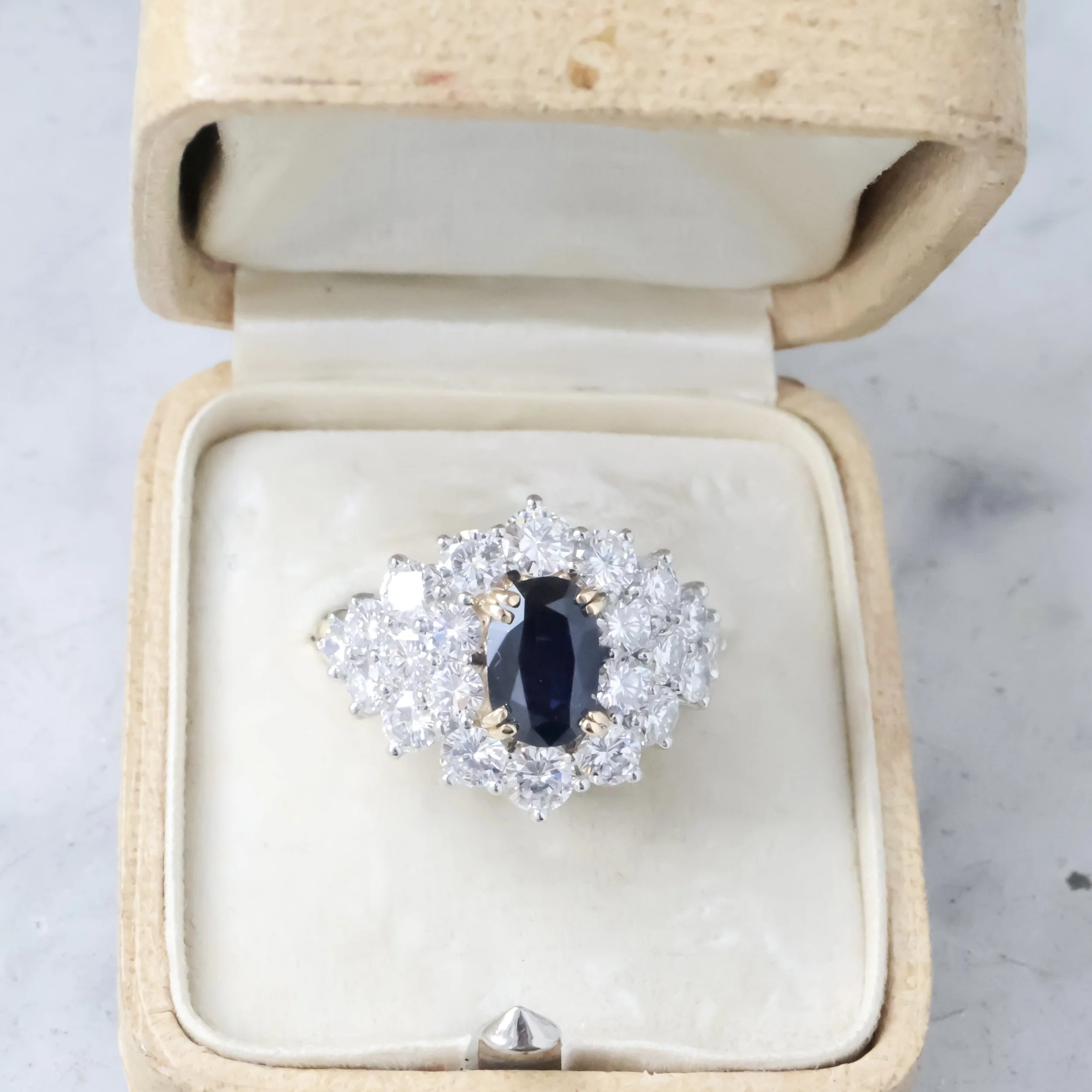 Bague avec un gros saphir noir au centre entouré de diamants dans une boîte en bois blanc