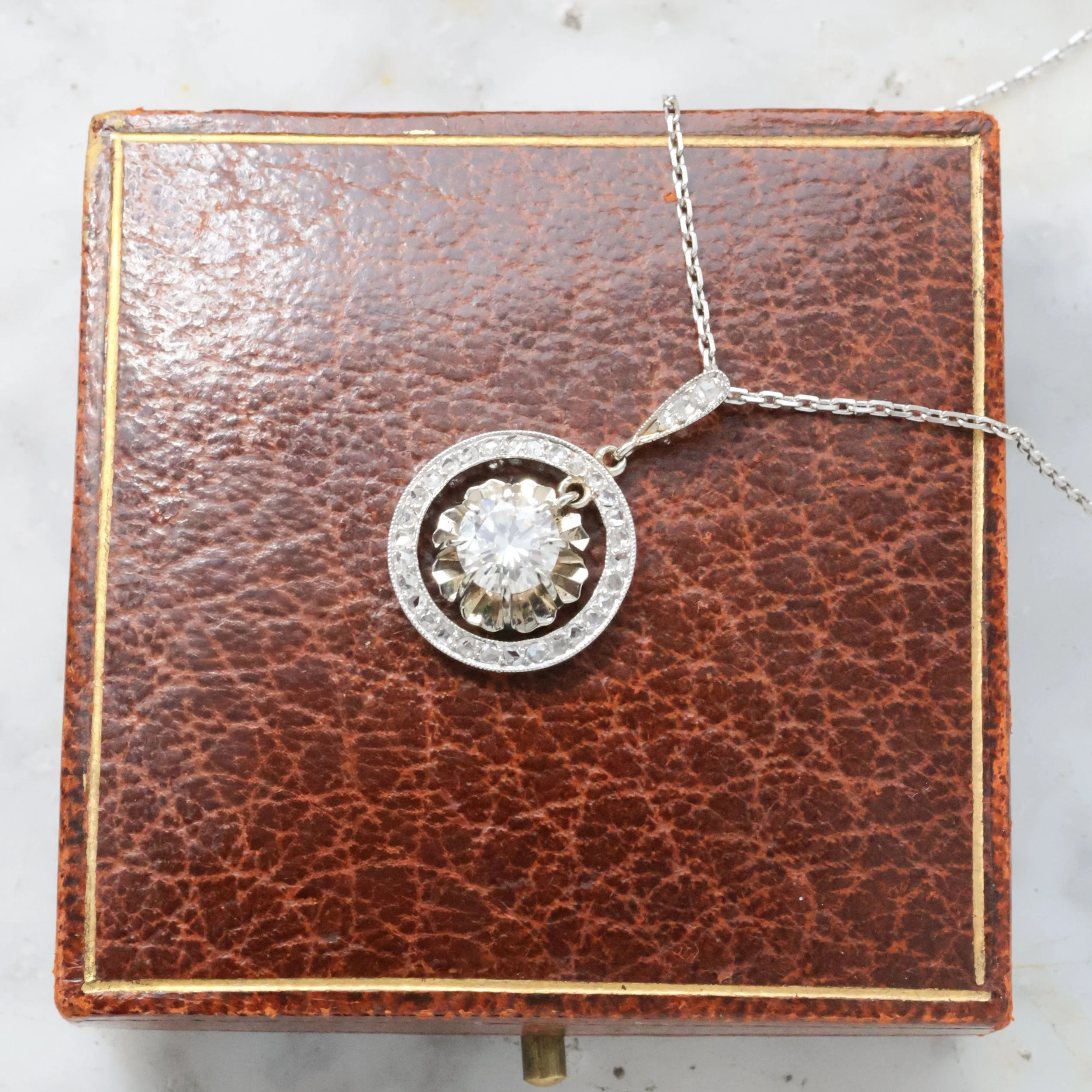 Une chaîne en argent avec un collier en pendentif rond orné de pierres ou diamants, posé sur un coffret en cuir marron.