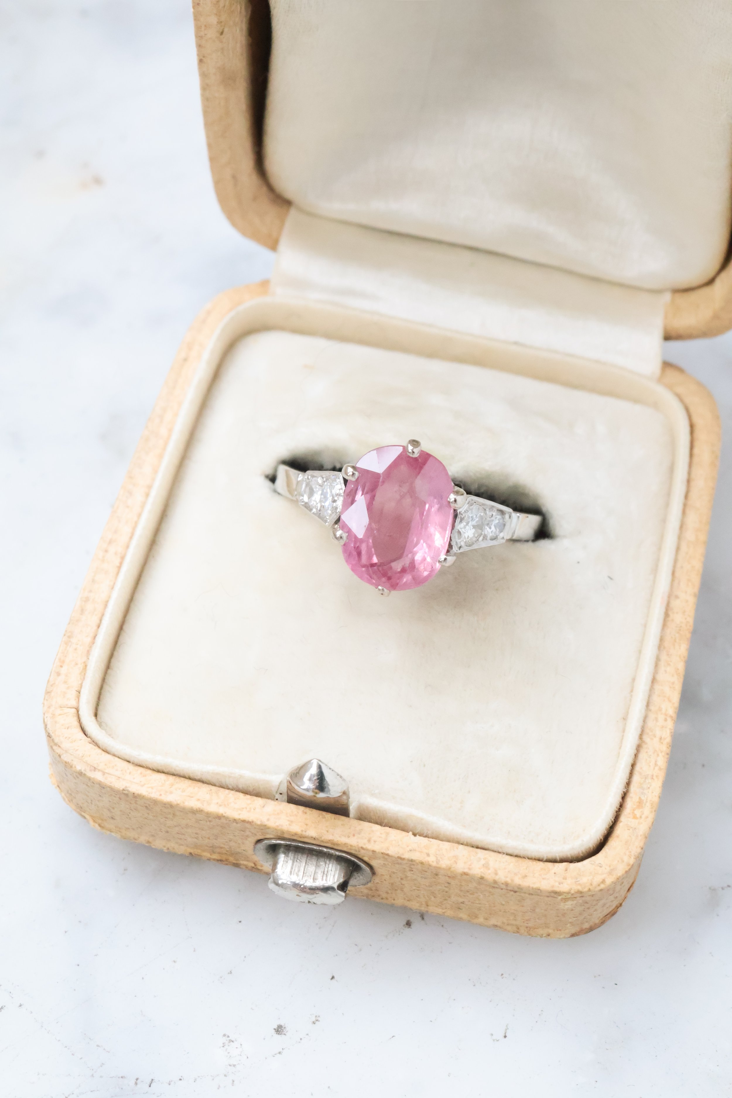 Bague avec pierre rose ovale et diamants dans une boîte en velours beige