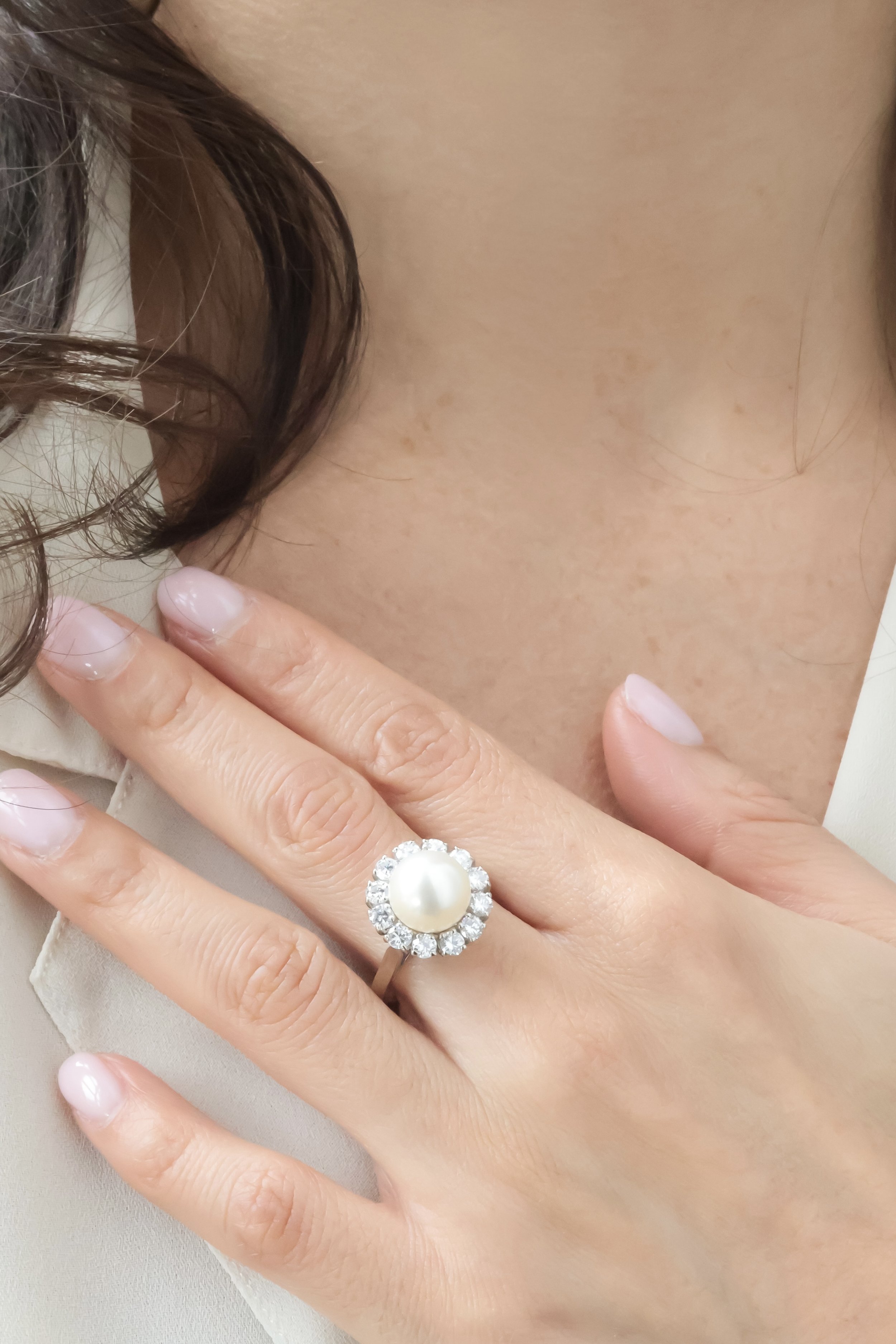 Une main portant une bague avec une perle centrale entourée de diamants, sur un doigt.