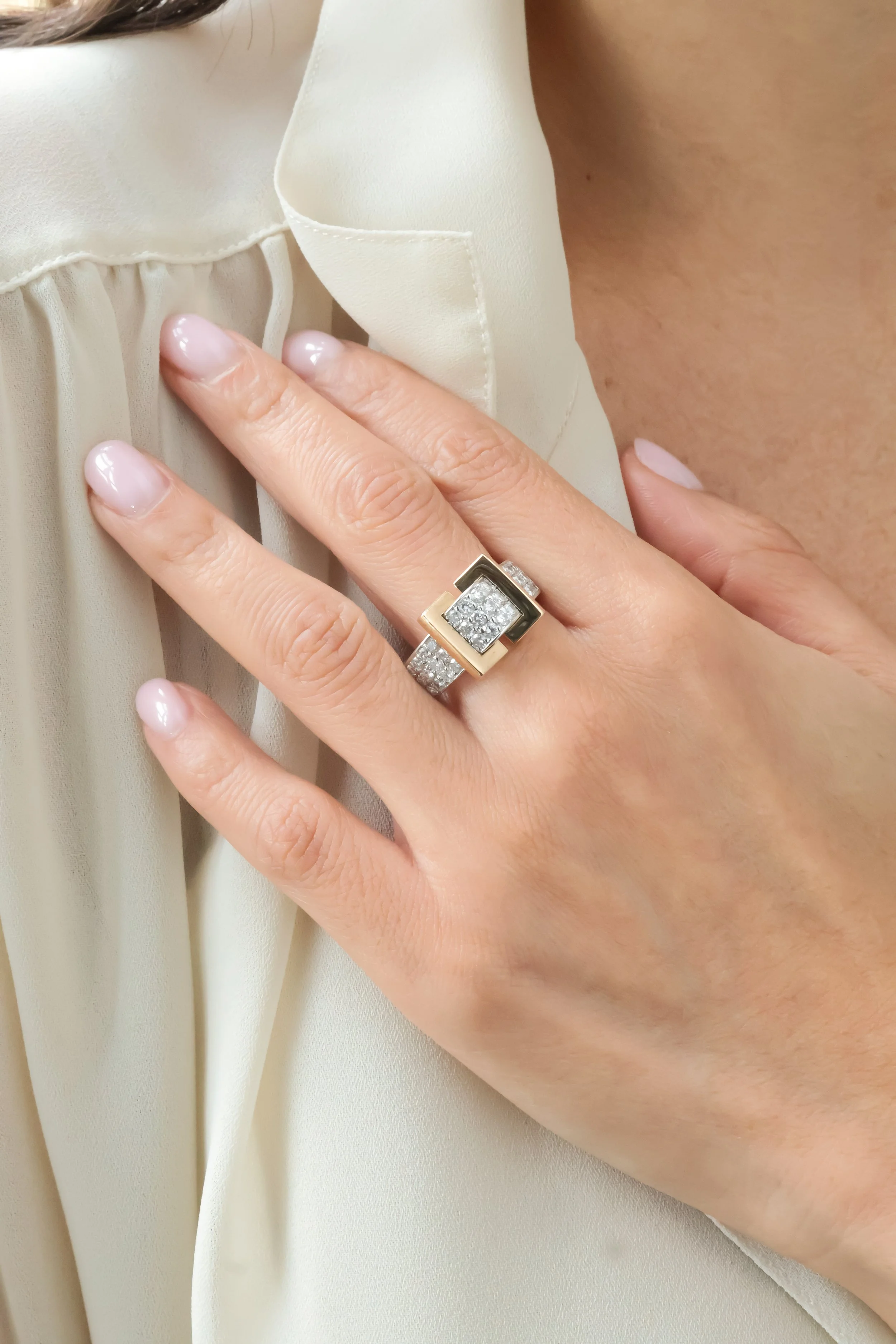 Une main avec une bague en or et en argent ornée de diamants, posée sur une blouse en satin beige.