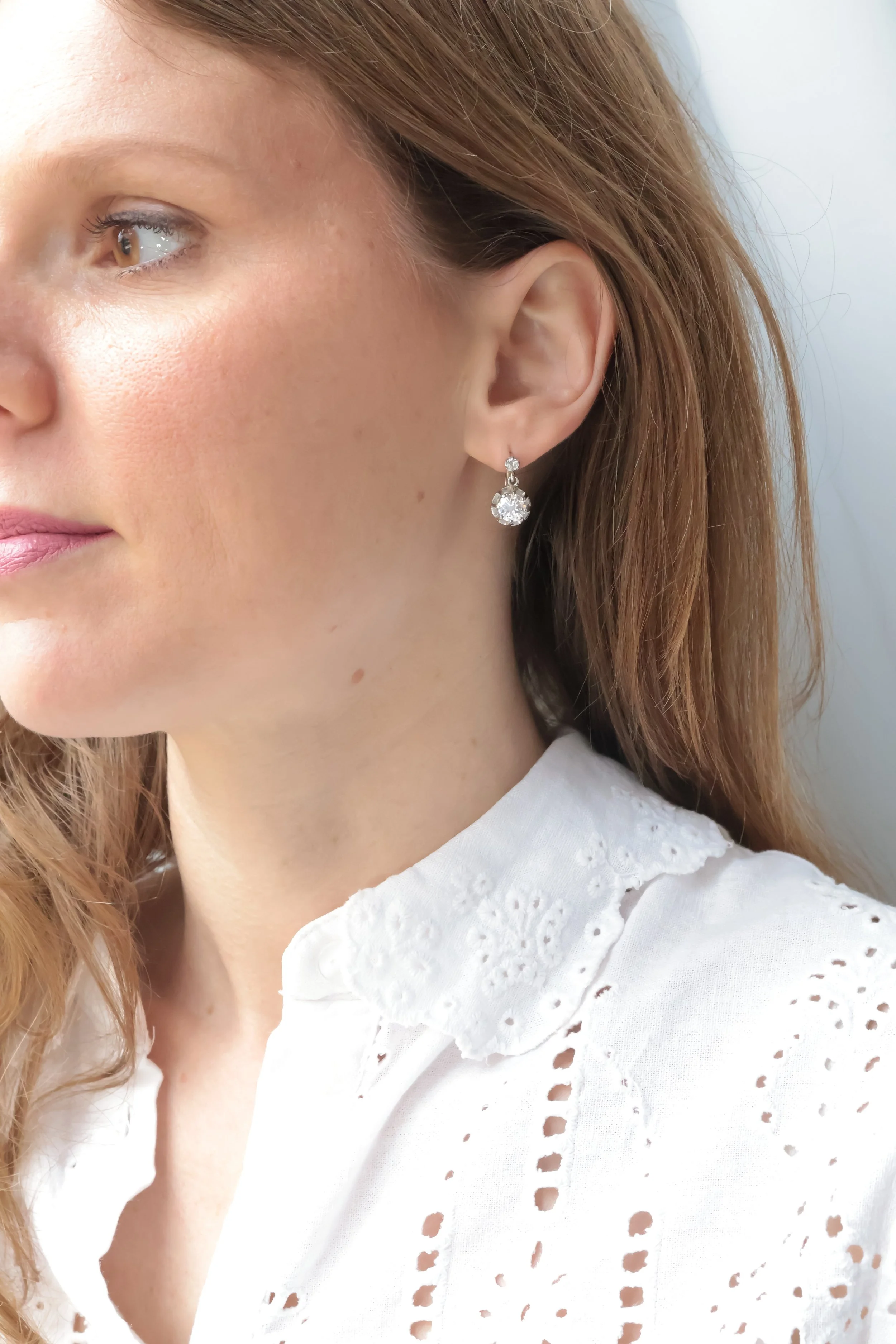 Vue de coté d'une femme avec des boucles d'oreilles dormeuses en diamant, portant un chemisier blanc en broderie.