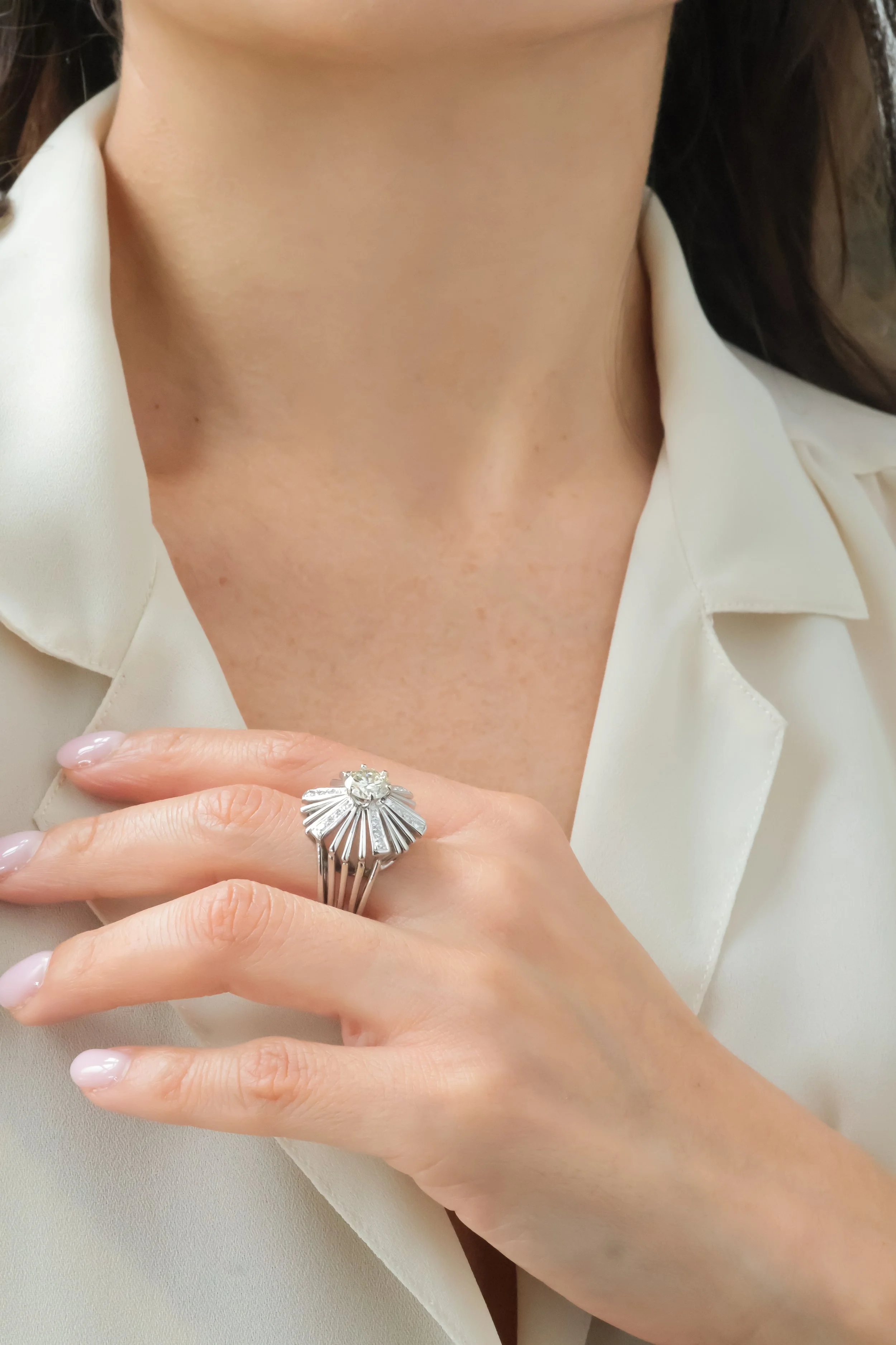 Une femme portant une chemise écrue, mettant en valeur une bague solaire vintage diamants sur le doigt.