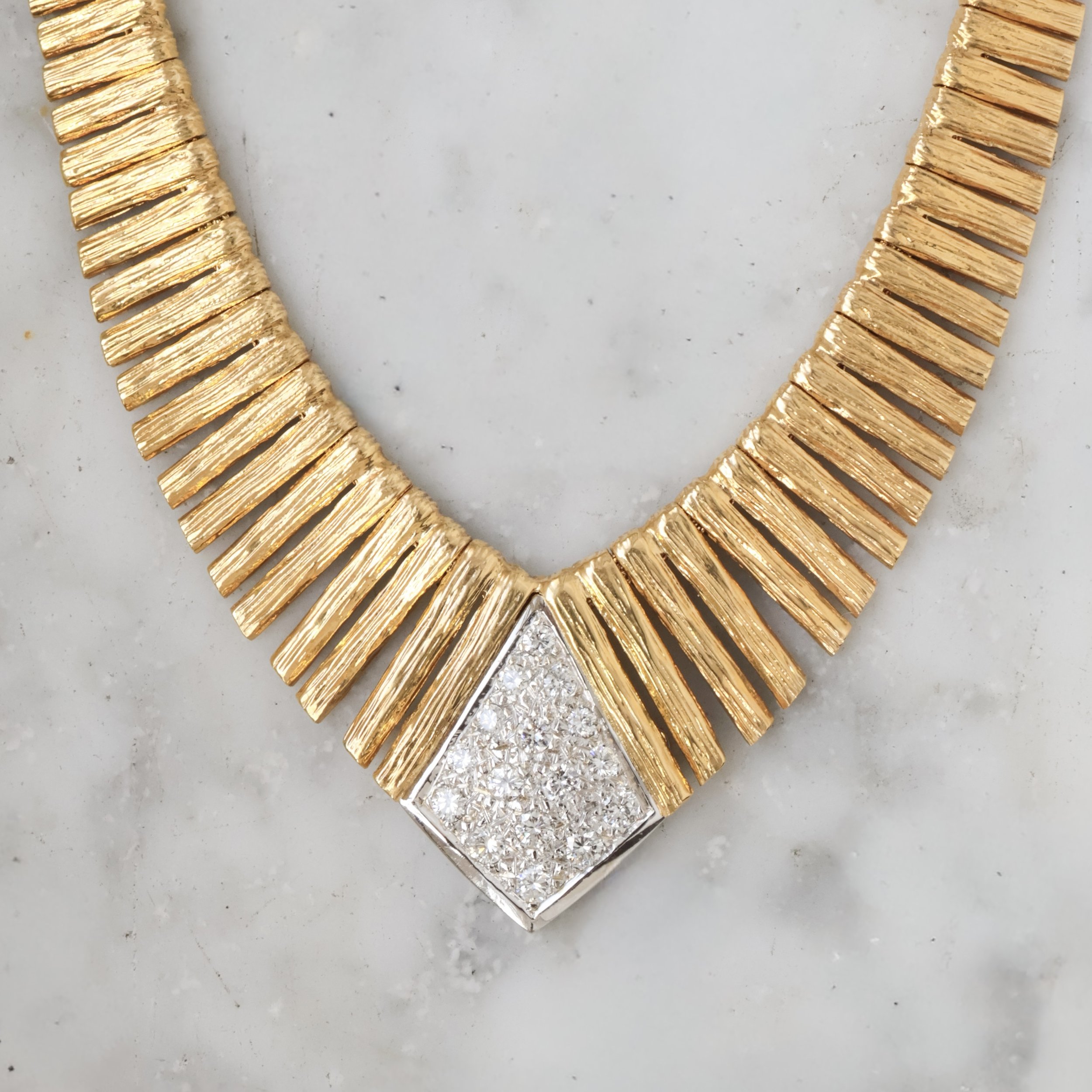Collier en or avec une pièce centrale pavée de diamants, sur une surface blanche.