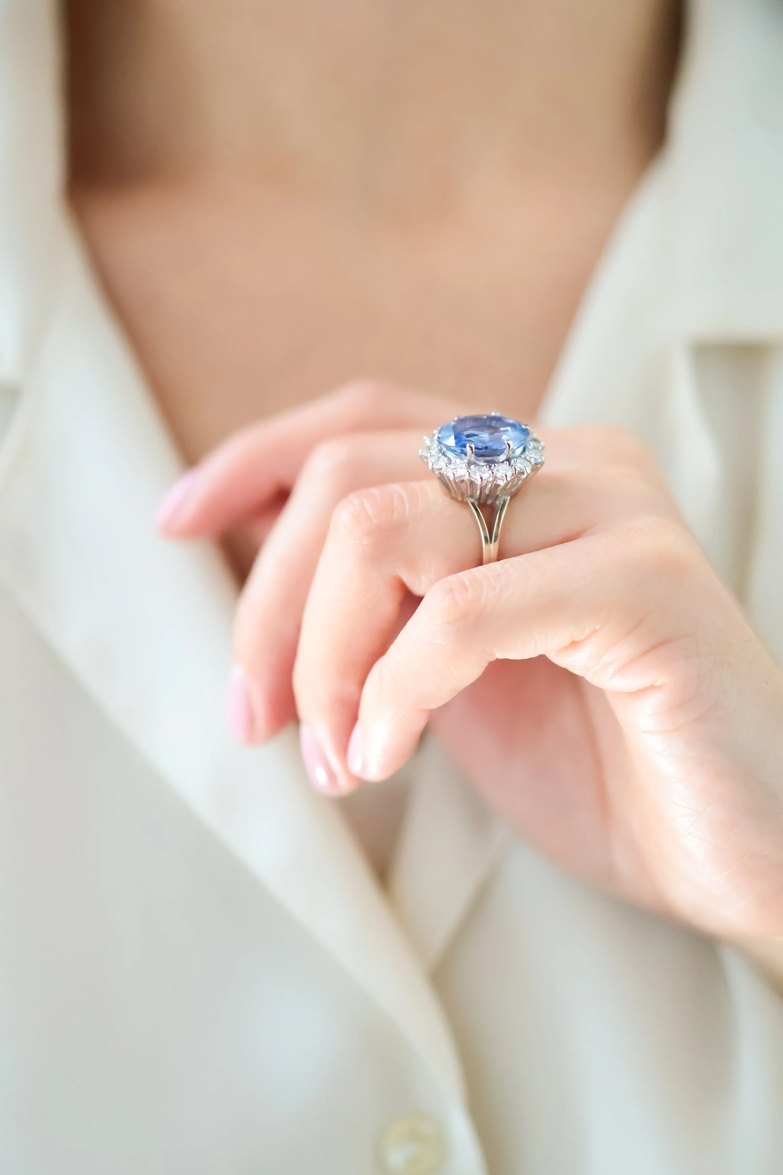 Une main portant une bague avec un grand saphir entouré de diamants, posée sur une peau nue.