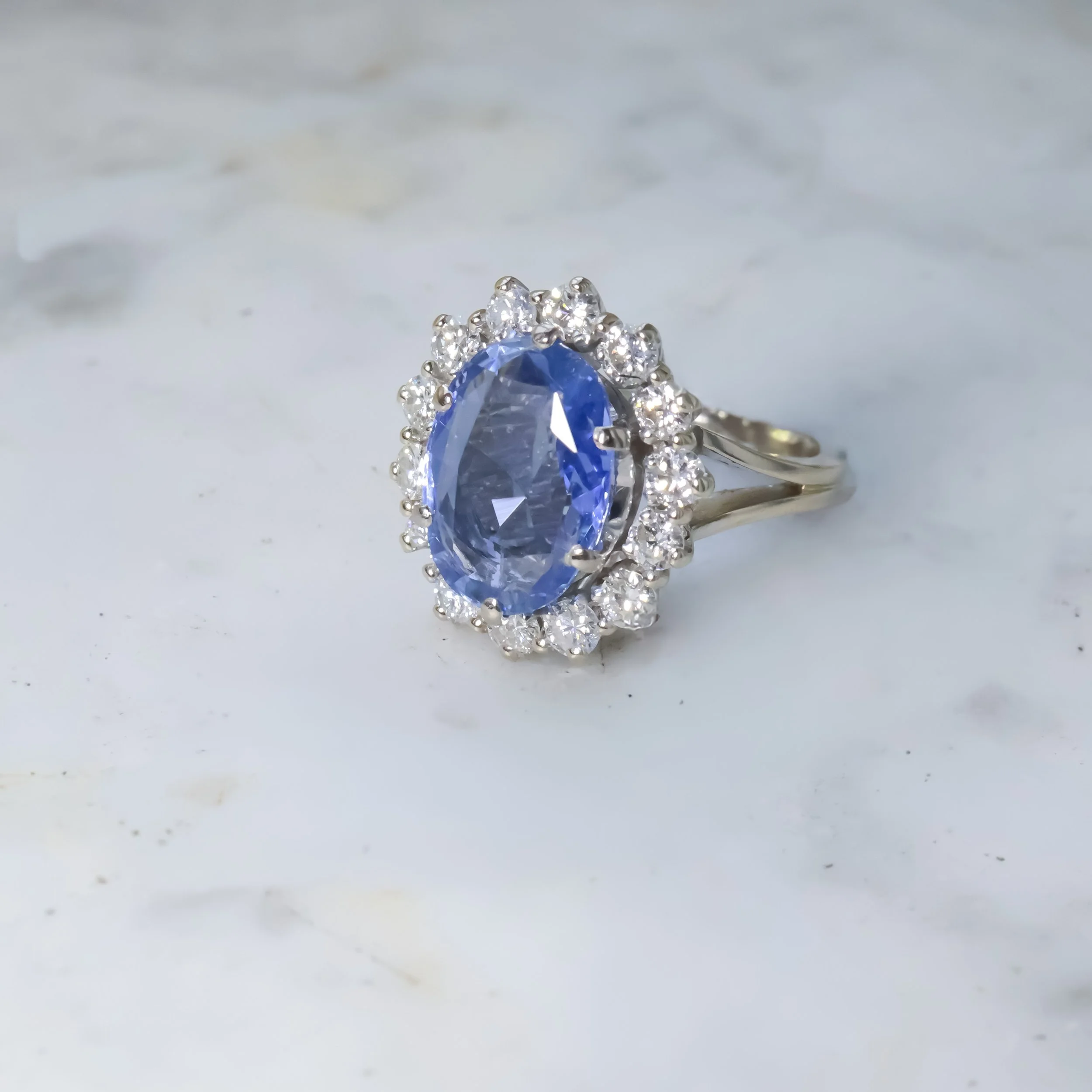 Bague en argent avec un grand quartz bleu oval entouré de diamants sur un fond blanc marble.