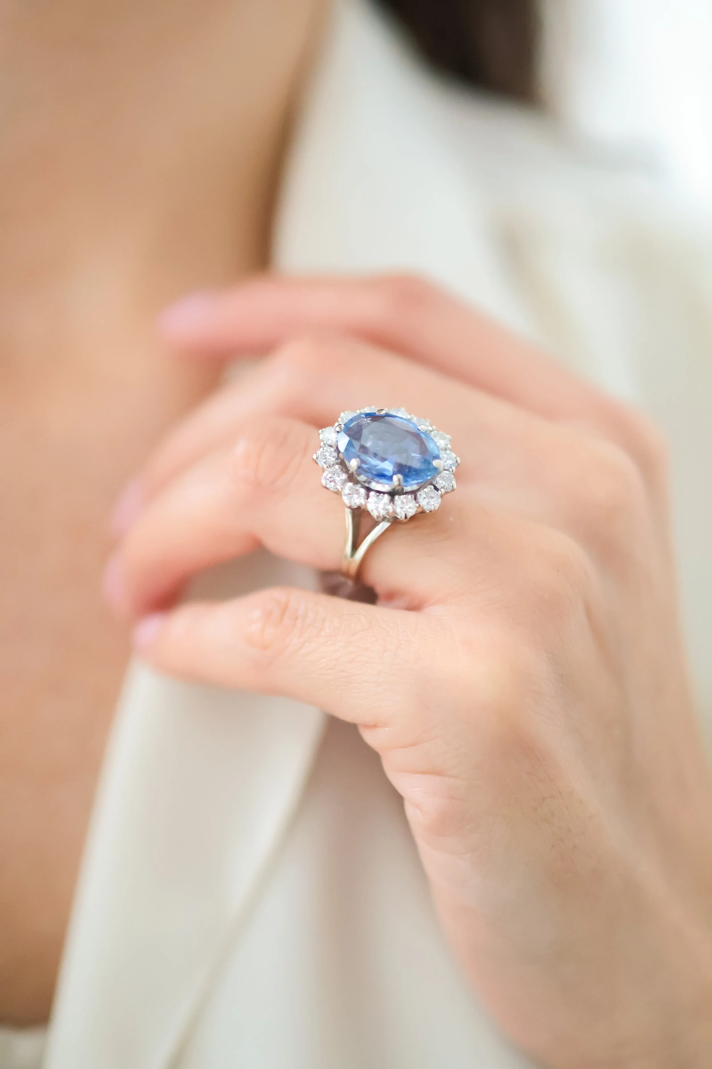 Une main portant une bague avec un grand pierre bleue entourée de diamants.