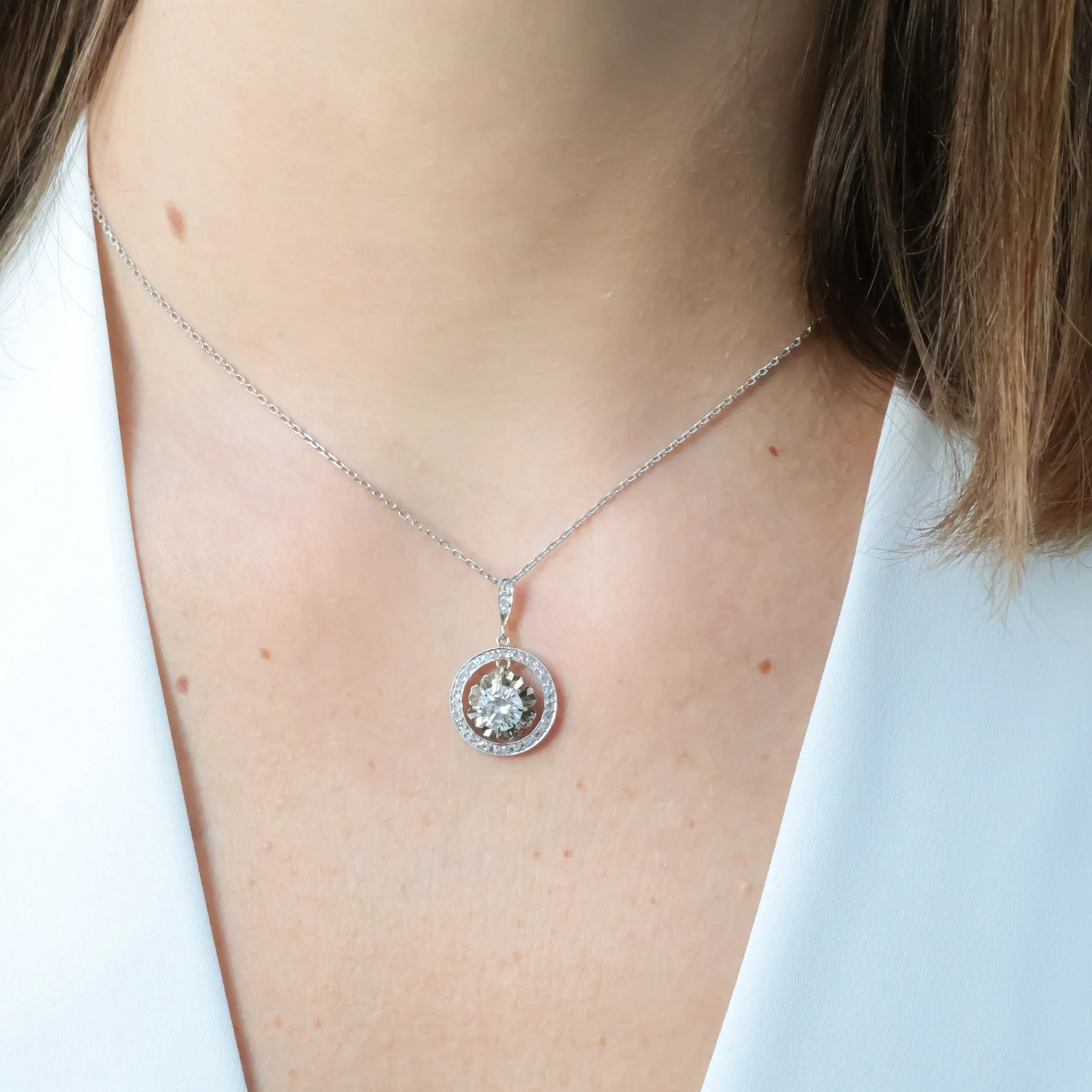 Collier en argent avec pendentif rond incrusté de pierres scintillantes, porté par une femme