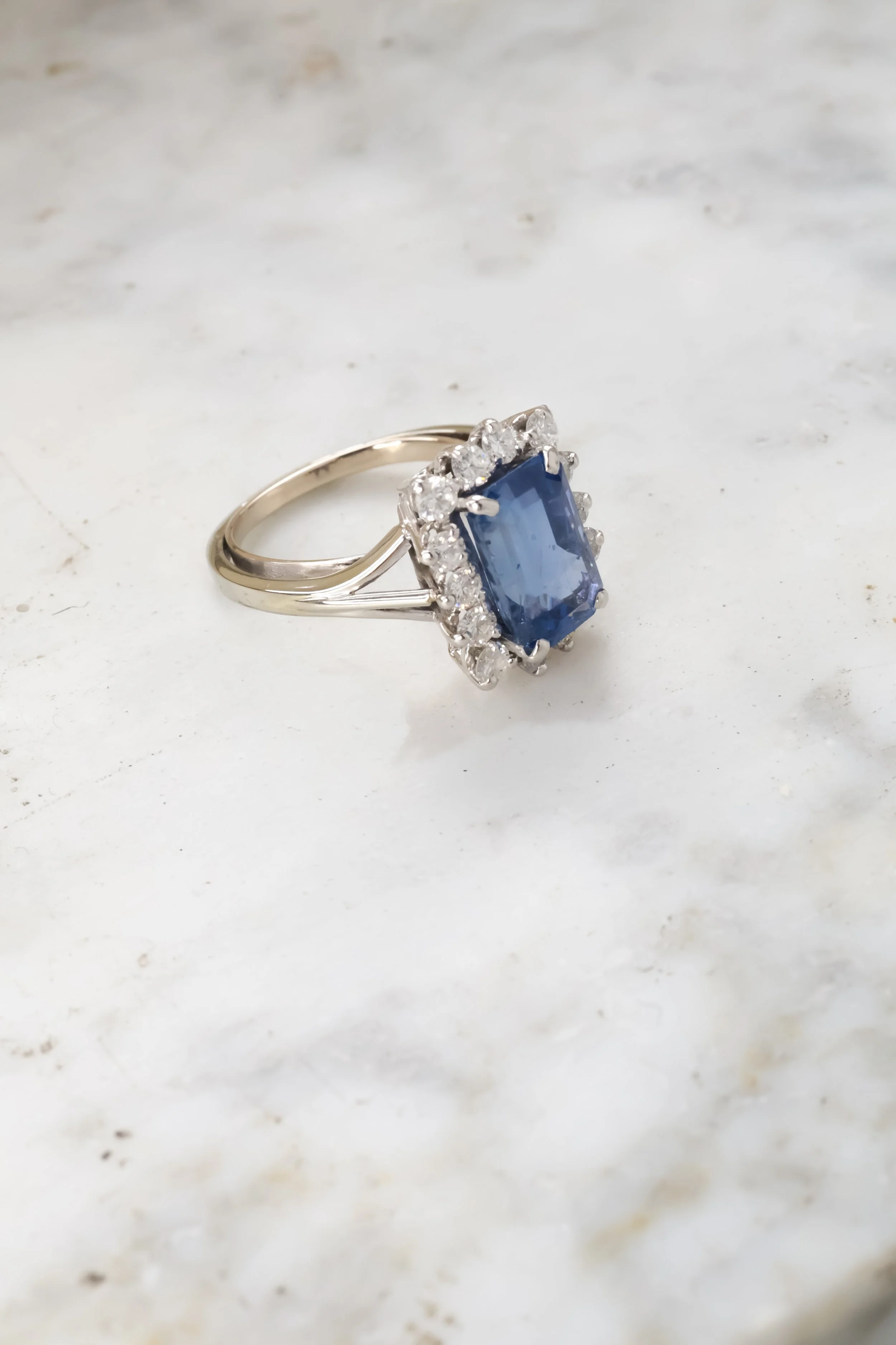 Bague avec un grand saphir bleu au centre entouré de diamants sur une surface blanche