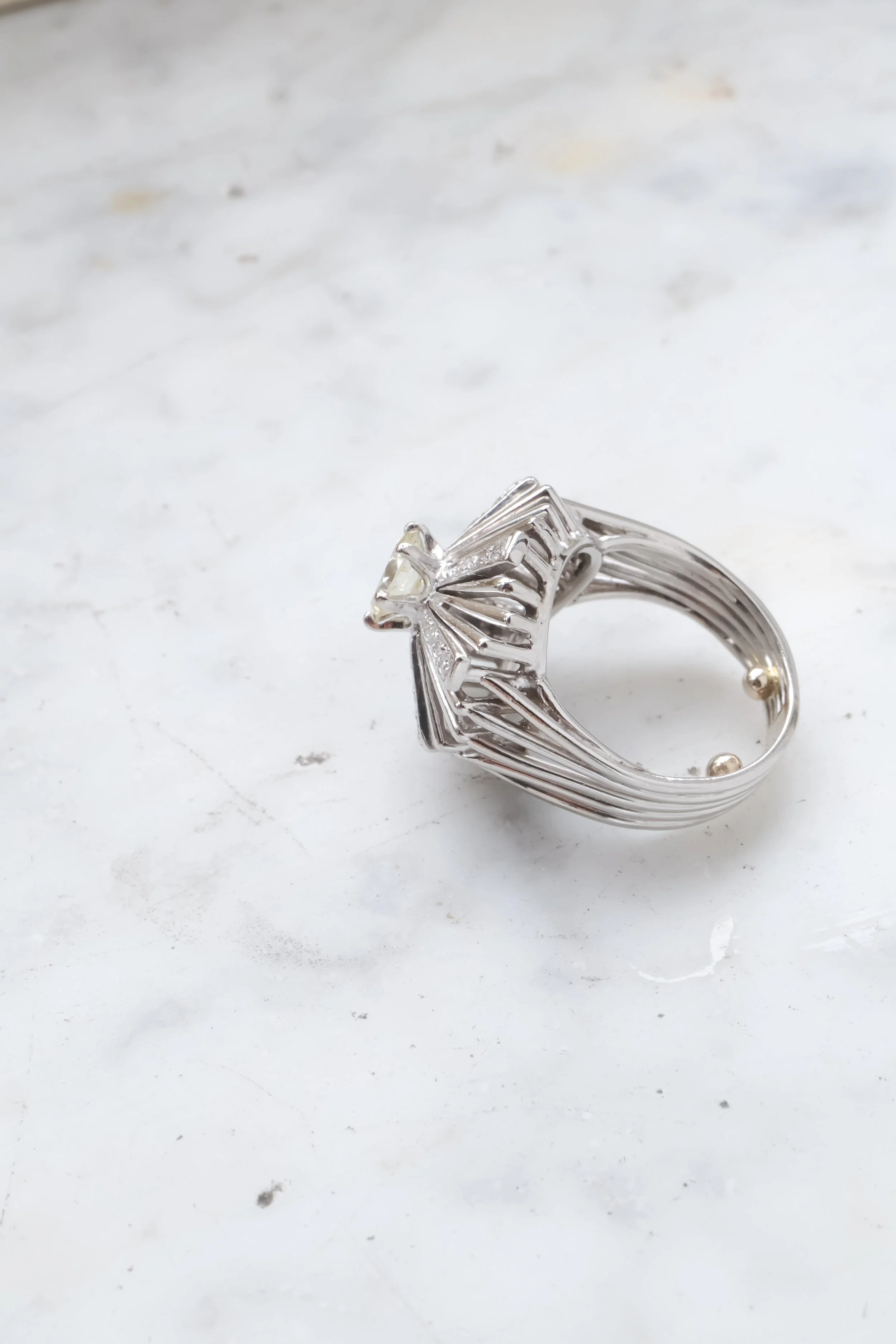 Bague en argent avec un design géométrique et une pierre au centre, posée sur une surface blanche