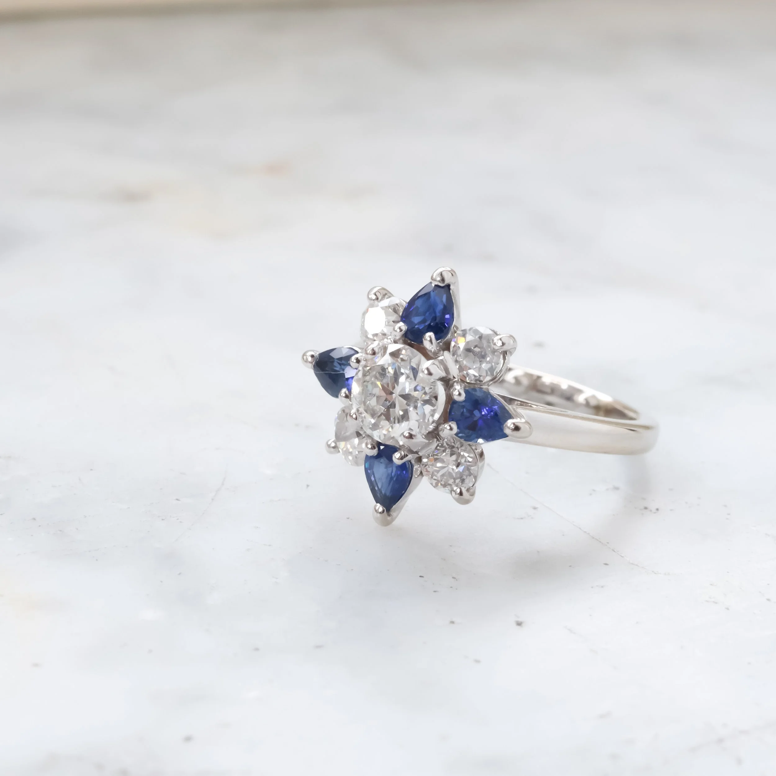 Bague en or blanc ornée de diamants et de saphirs bleus posée sur du marbre 