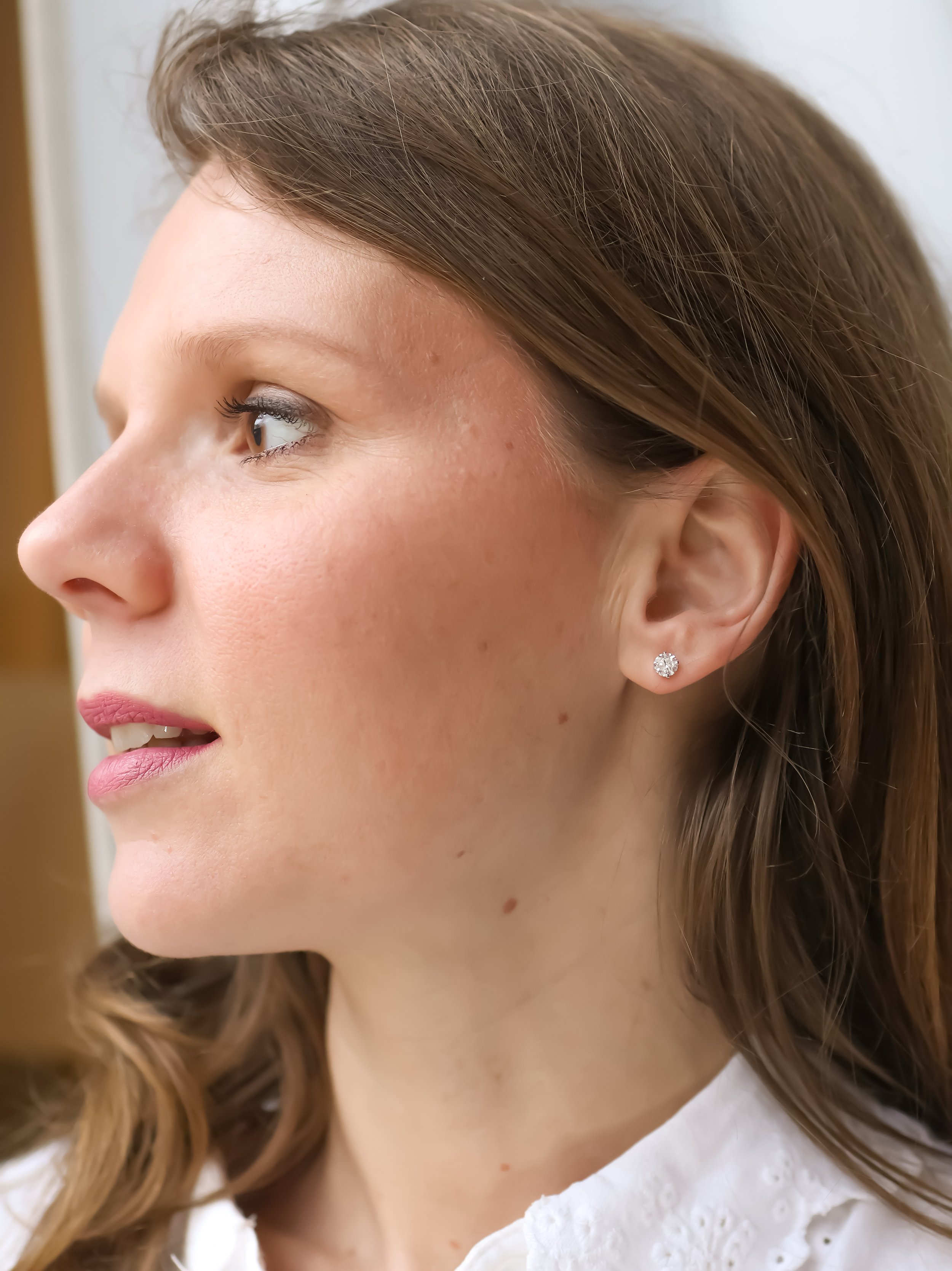 Profil d'une femme avec des boucles d'oreilles en diamant, peau claire, cheveux blond, maquillage naturel, portant une chemise blanche, regardant vers la gauche.