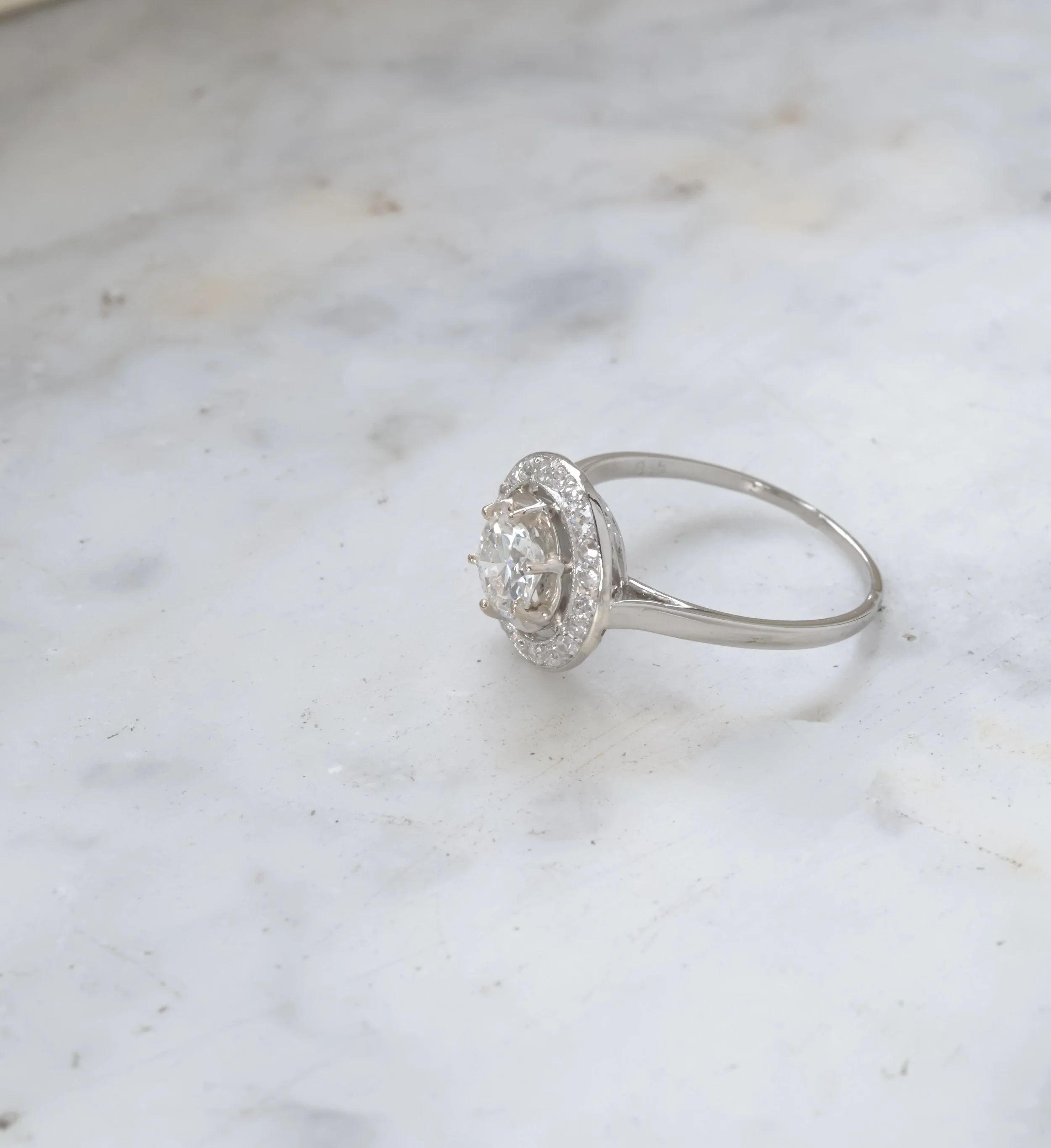 Bague en argent avec un grand diamant rond entouré de petits diamants sur une surface blanche