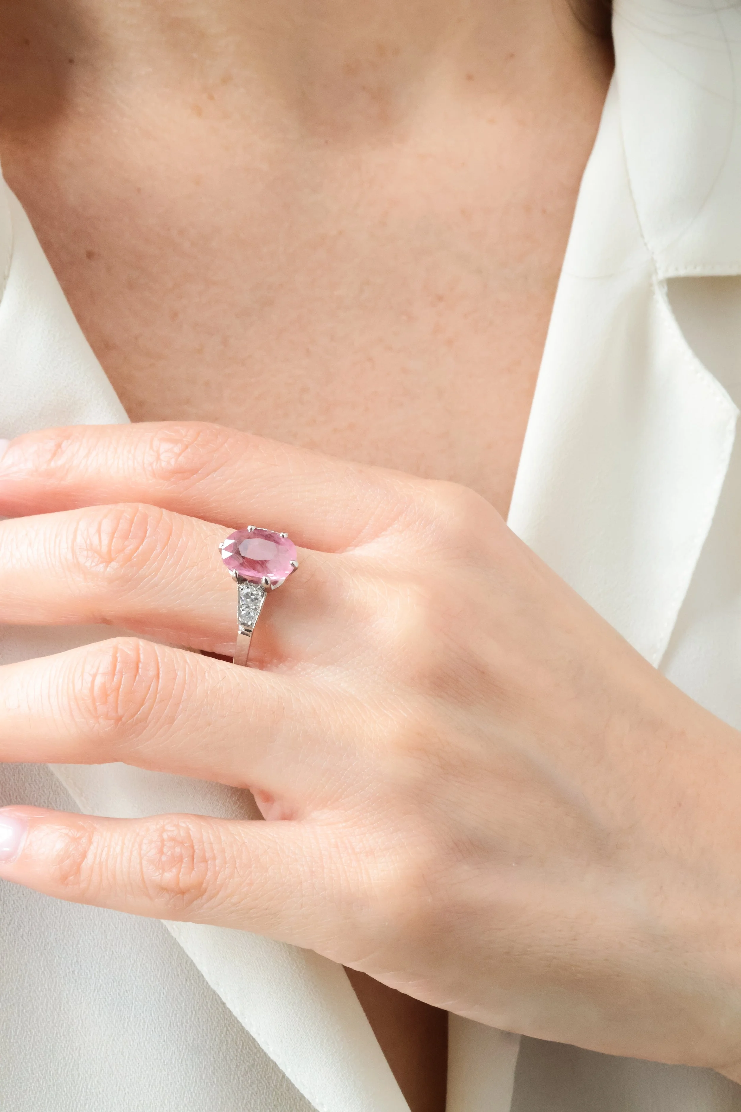 Une main portant une bague avec une pierre rose et quelques petits diamants sur un doigt.