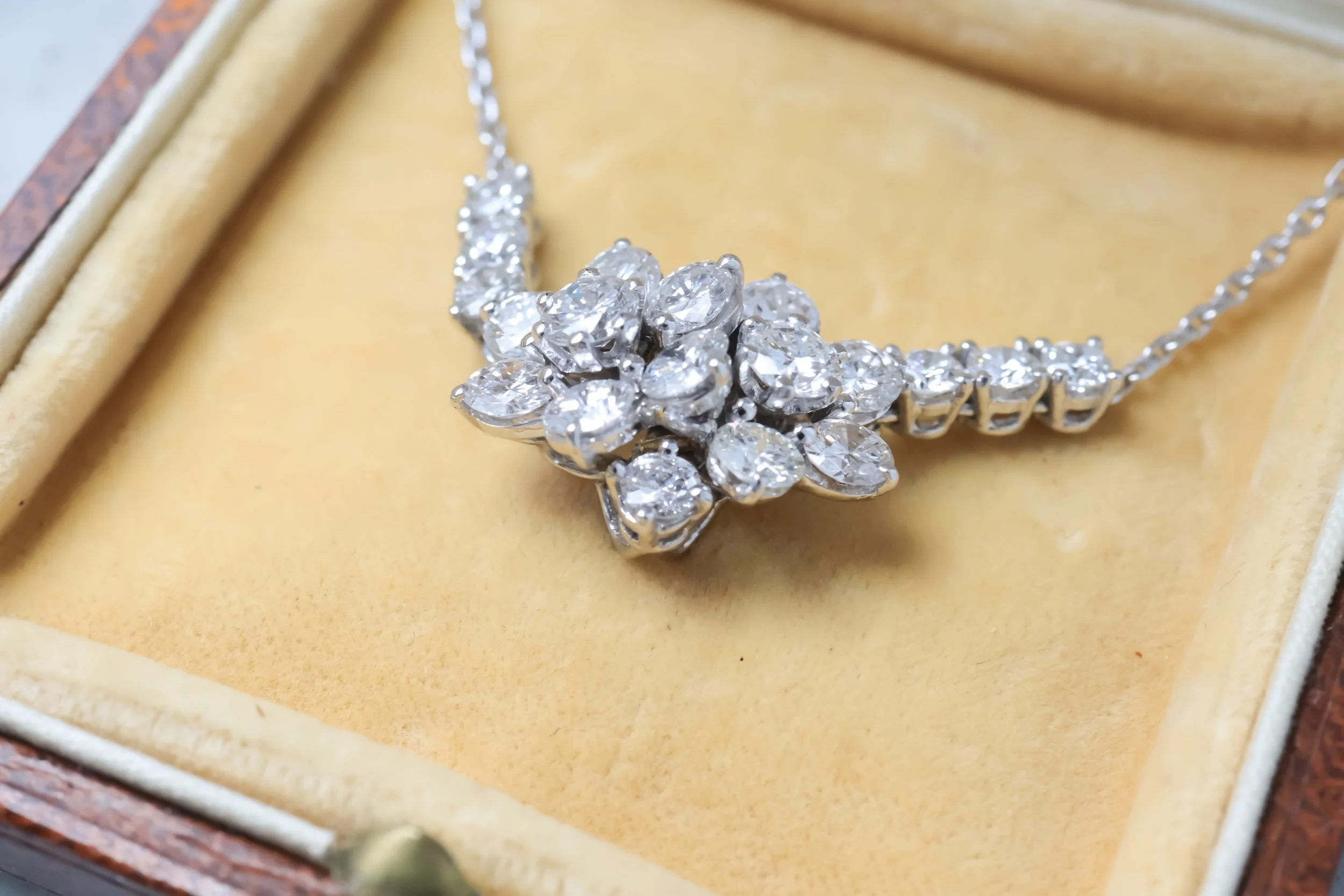 Collier en argent avec une pièce centrale ornée de diamants, présenté dans une boîte en bois avec un coussin en velours beige.