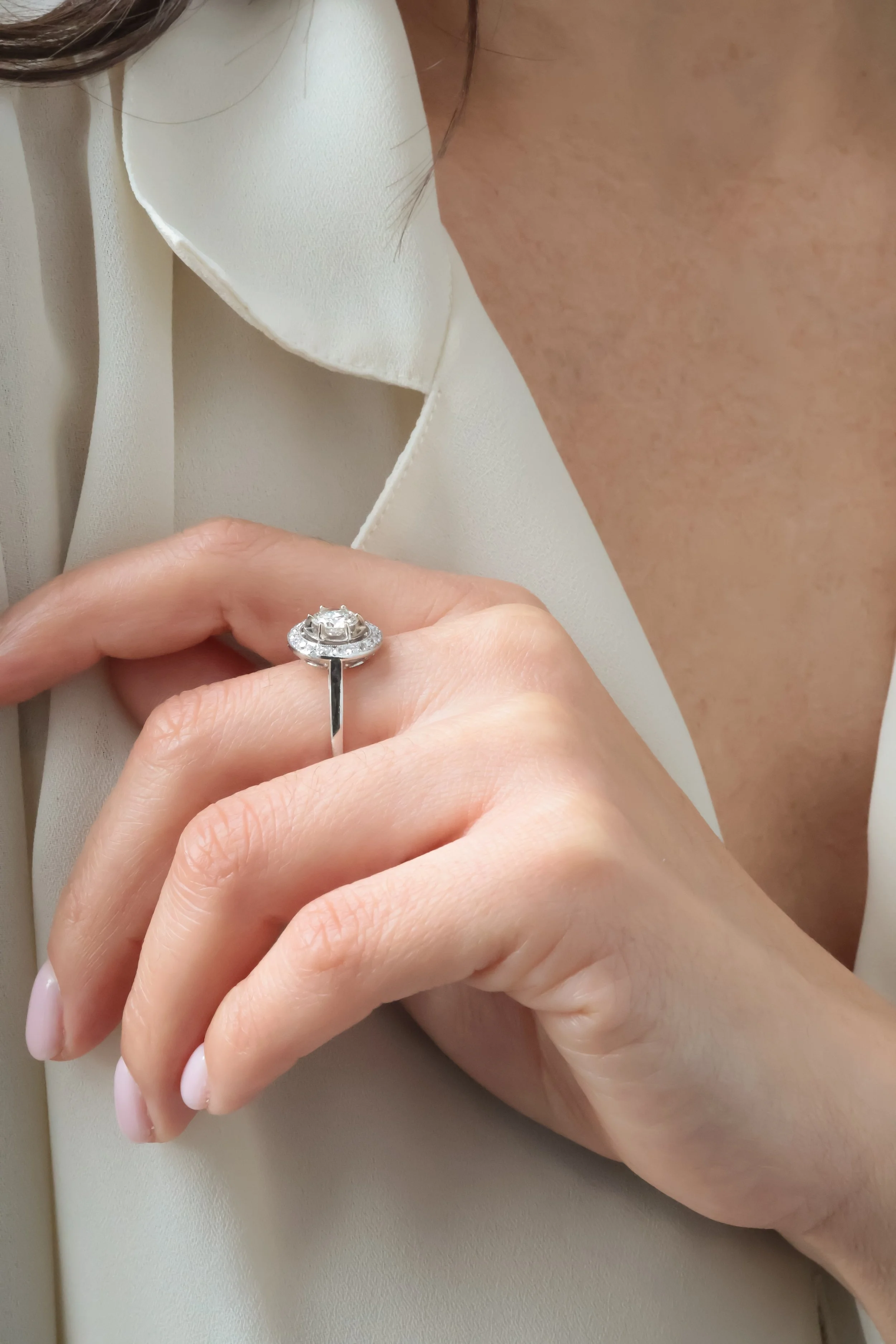 Une personne porte une bague en argent avec une pierre précieuse au doigt, vêtue d'une chemise blanche en tissu léger.